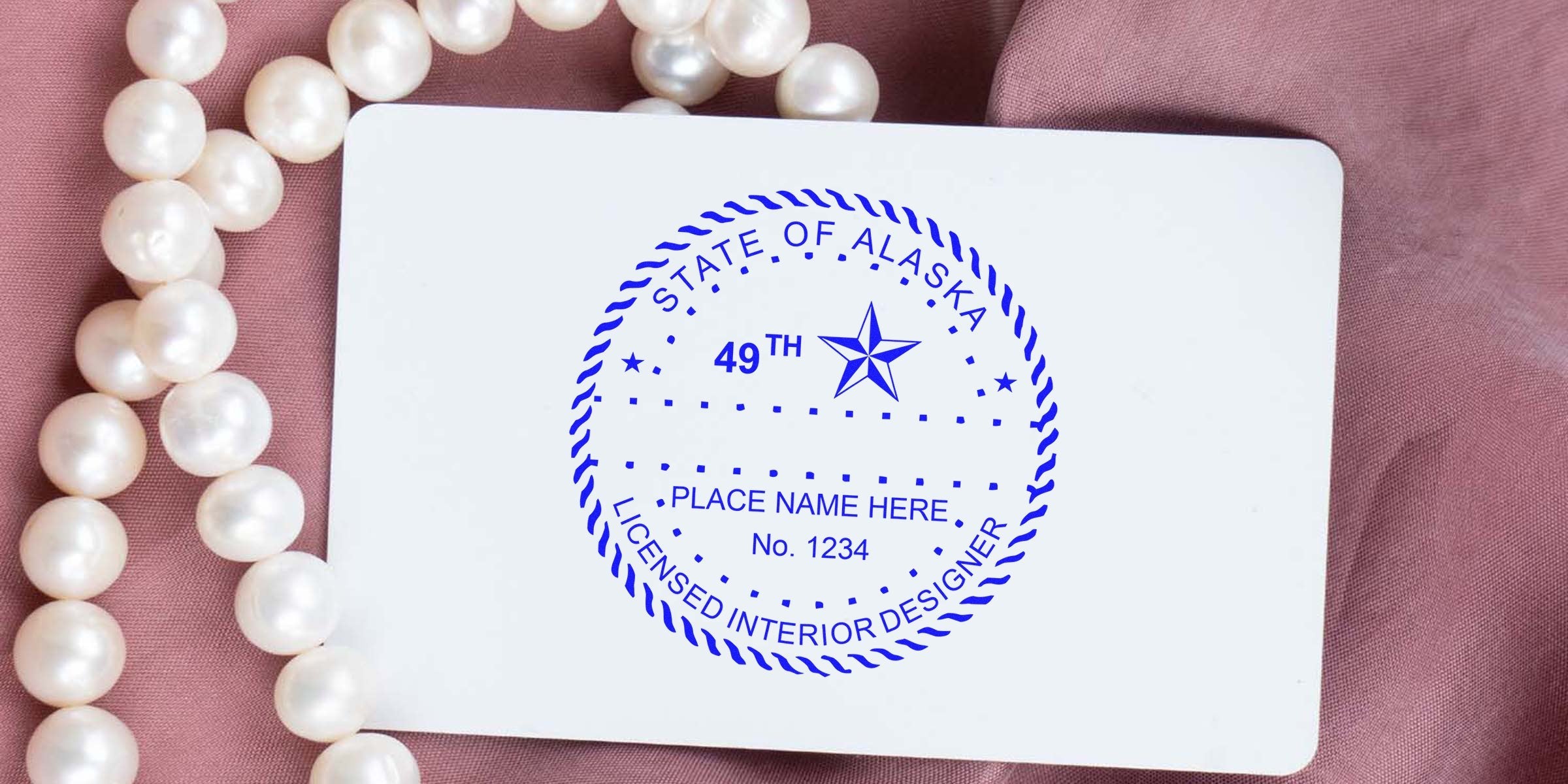 Alaska interior designer stamp on white card with pearl necklace and pink fabric, symbolizing choosing an interior designer in Alaska.