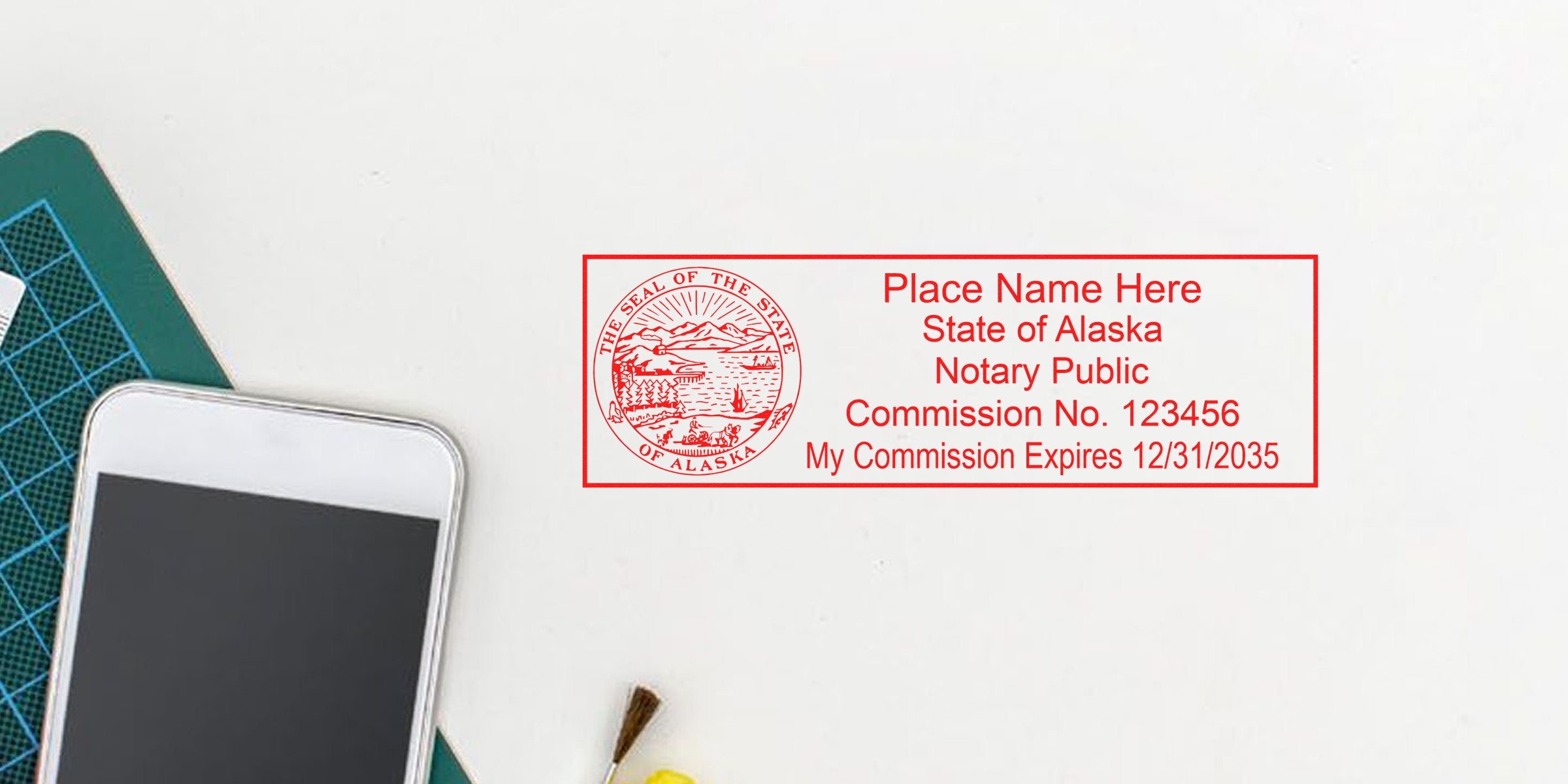 Alaska notary stamp with commission number and expiration date on white background next to smartphone and cutting mat, showing Alaska notary stamp rules and seal regulations.