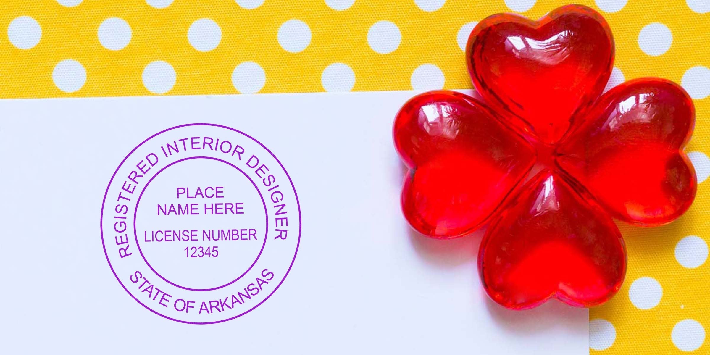 Red heart-shaped glass on white paper with Arkansas interior designer license stamp, meeting Arkansas design stamp requirements, against a yellow polka dot background.