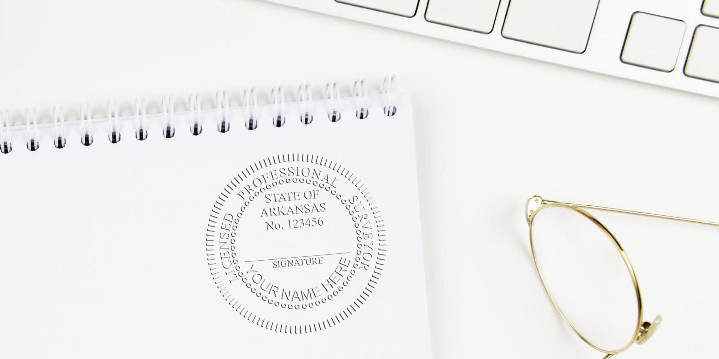 Arkansas land surveyor stamp on white notepad with keyboard and glasses, showing licensed professional surveyor seal and highlighting benefits of self-inking stamp.