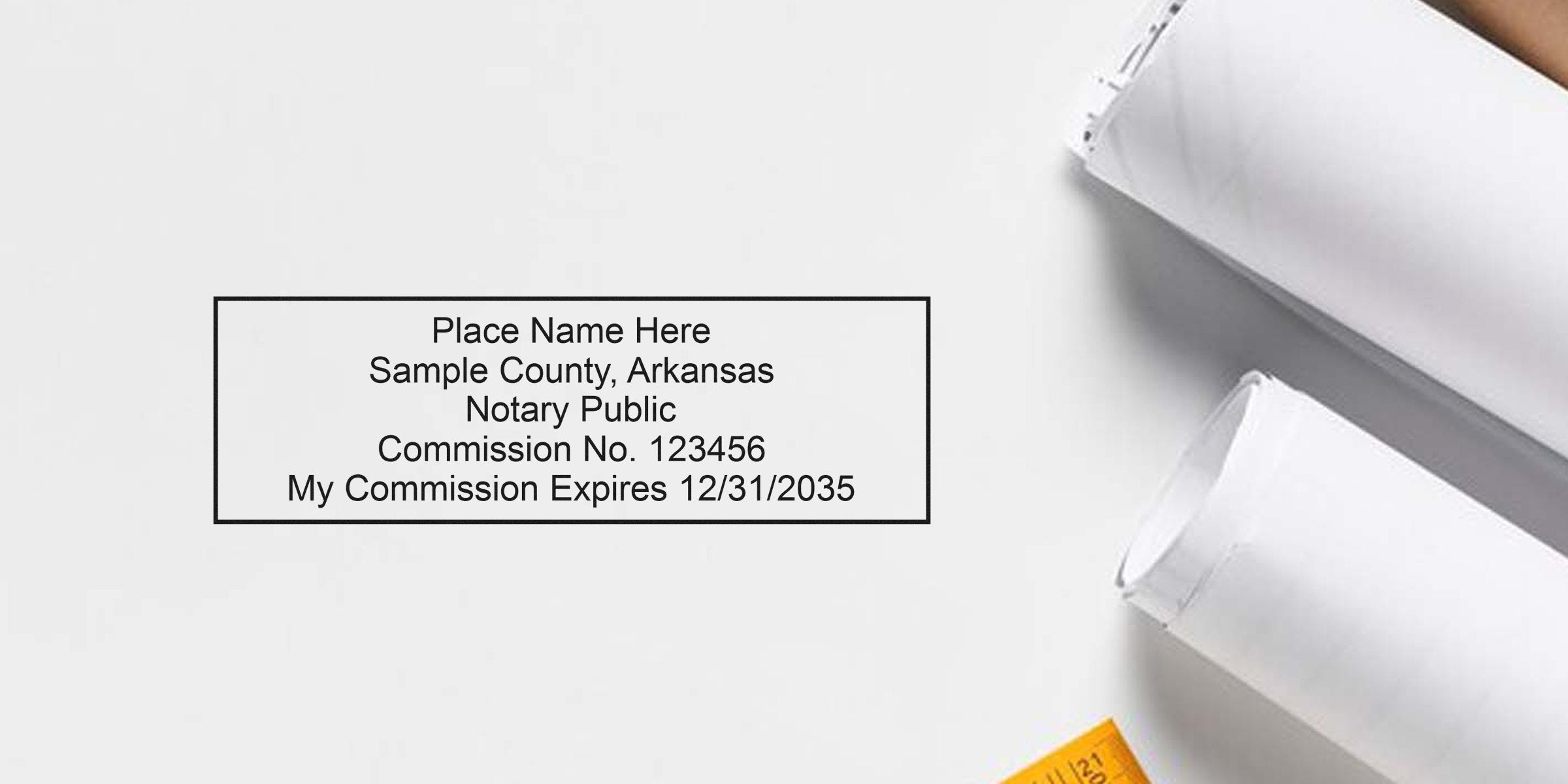 Arkansas notary kit with a notary public stamp sample showing commission expiration date, plus rolled blueprints and essential notary supplies.