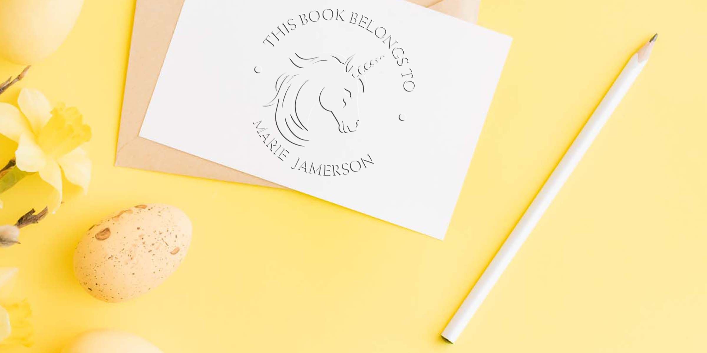 Personalized unicorn bookplate card with the name Marie Jamerson, arranged on a yellow Easter-themed background with a pencil, flowers, and speckled egg