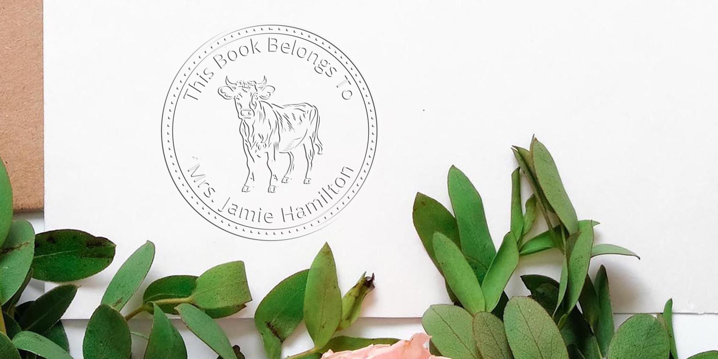 Personalized bookplate with cow illustration and “This Book Belongs To Mrs Jamie Hamilton” text on white paper, framed by green leaves