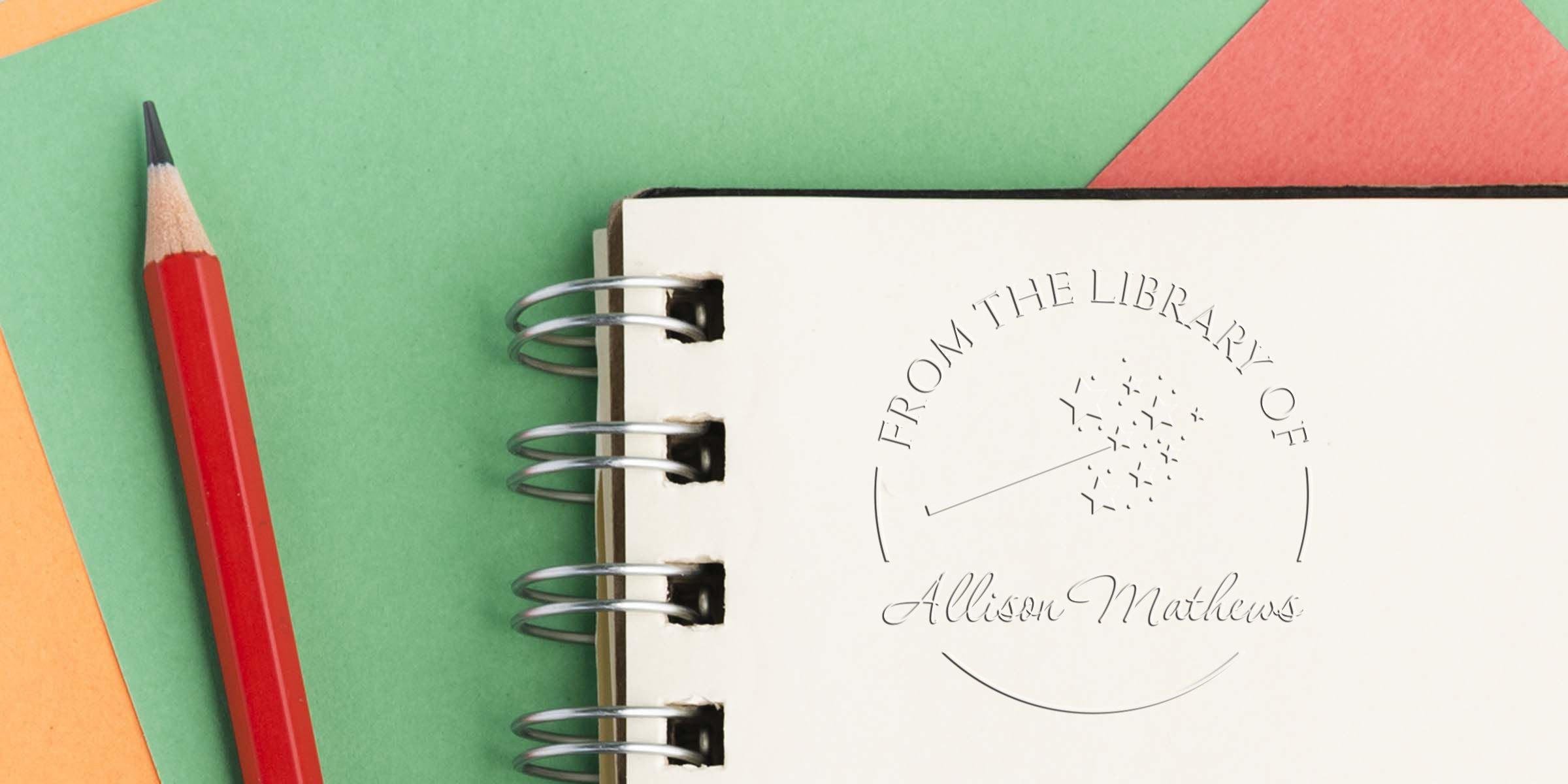 Red pencil beside a spiral notebook with “From the Library of Allison Mathews” embossed on the cover over colorful paper background
