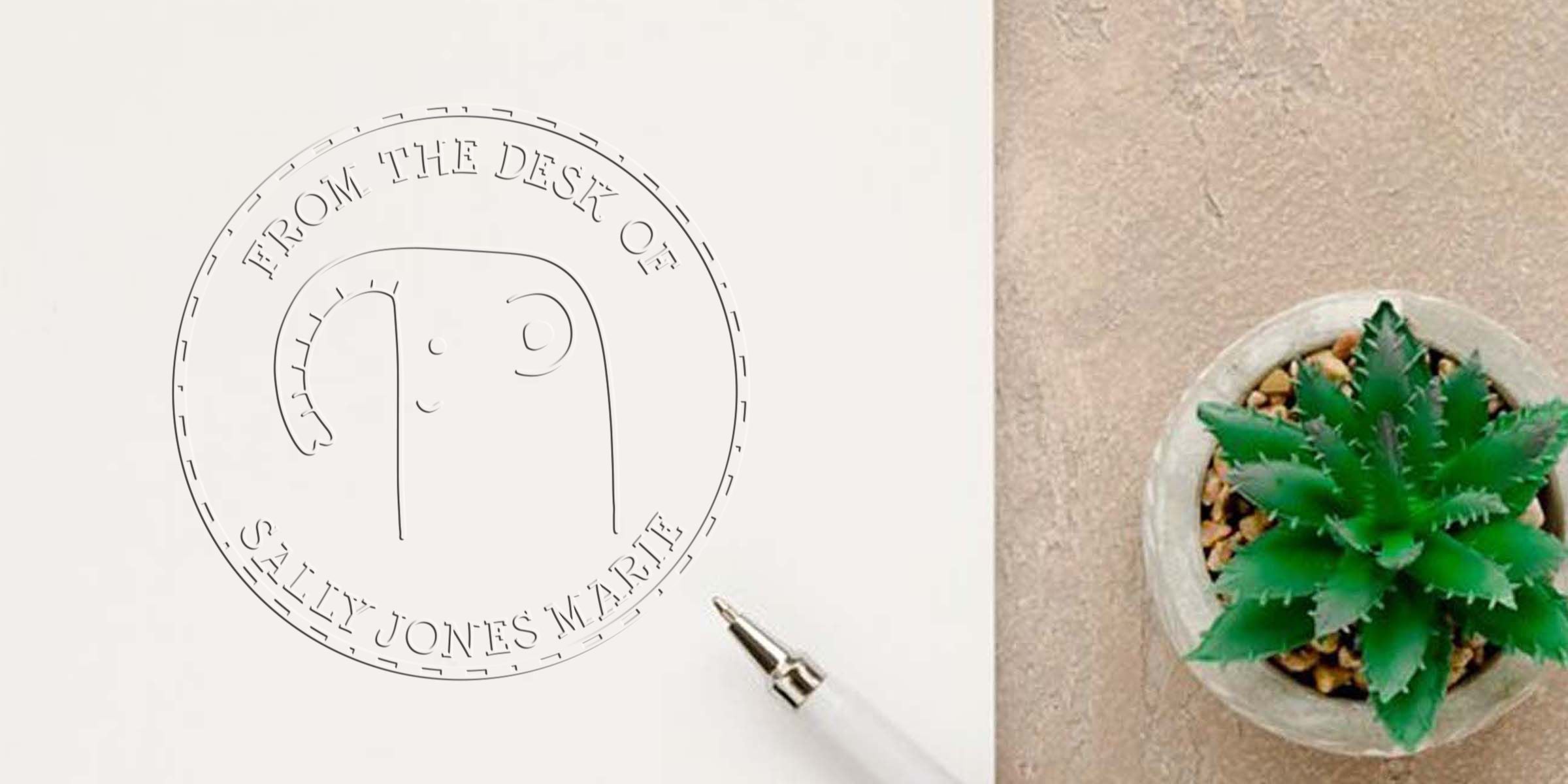 Custom embossing seal imprint reading “From the Desk of Sally Jones Marie” on white paper beside a small potted succulent plant.