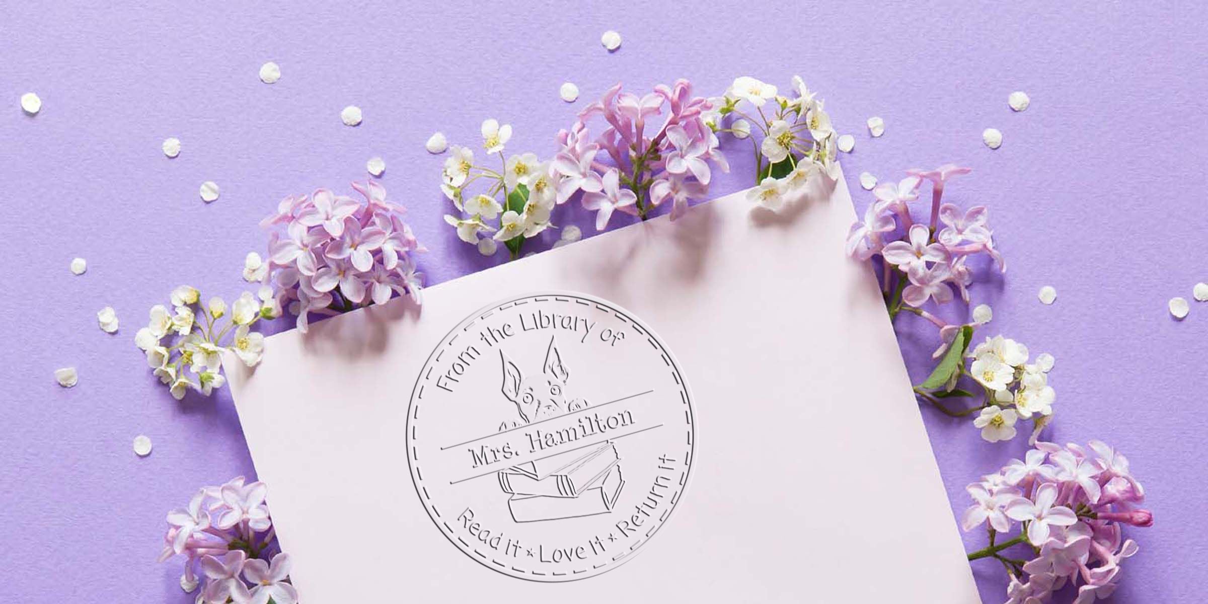 Elegant lilac flowers and confetti around a pink stationery card featuring a Mrs. Hamilton library stamp logo on a lavender background