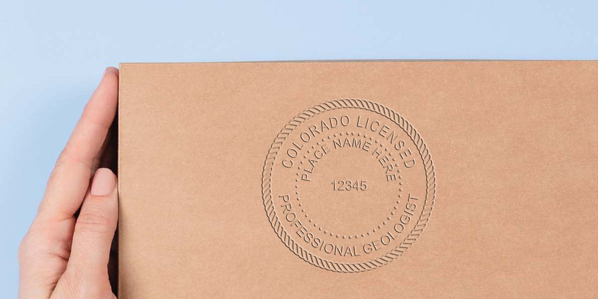 Hand holding a cardboard box with an embossed Colorado geologist seal, certification number, and detailed seal design.