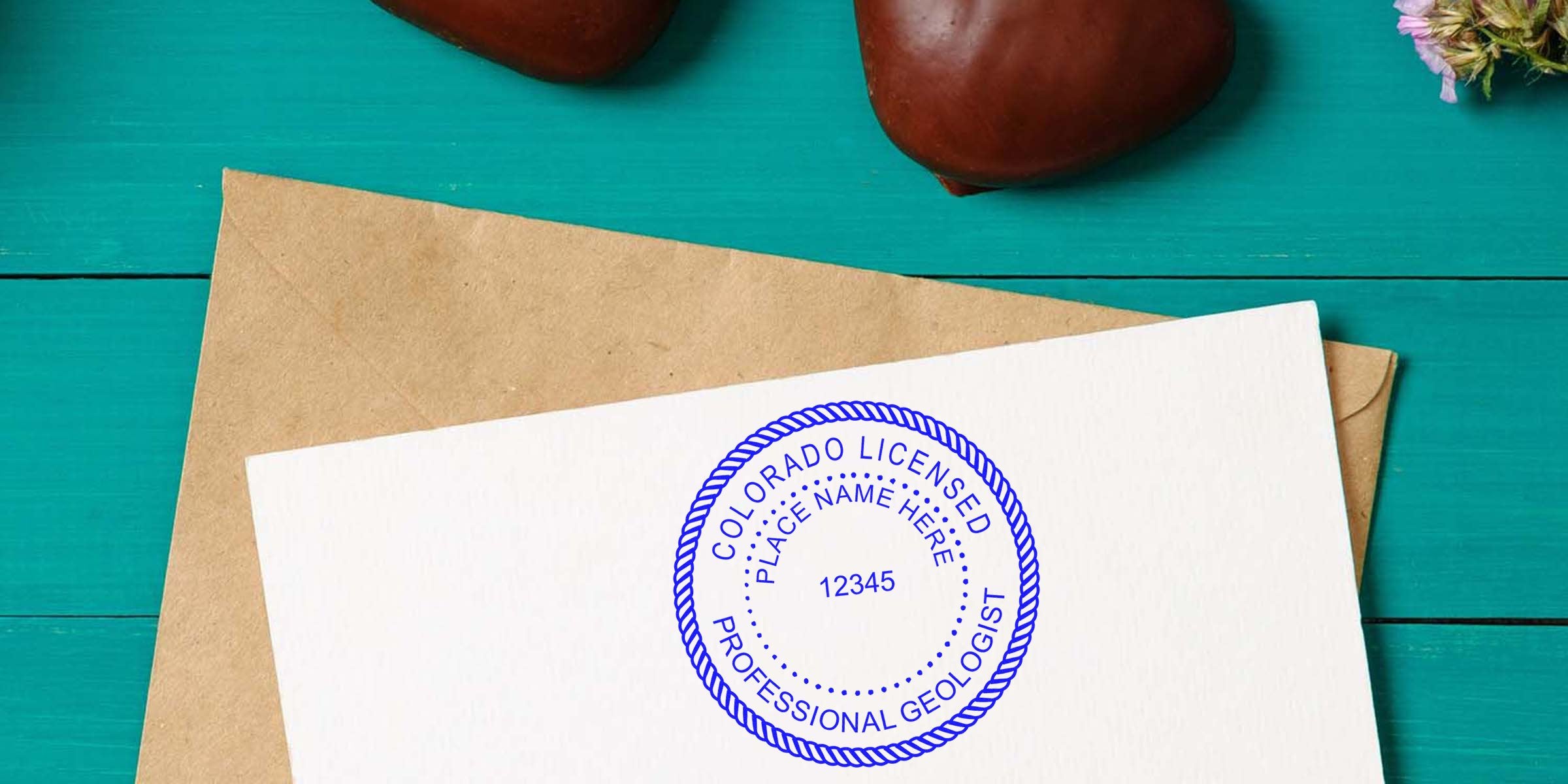 Colorado geologist seal template with licensed professional geologist stamp on white paper, plus envelope and heart-shaped stones on turquoise wood, designed to simplify geologist tasks.