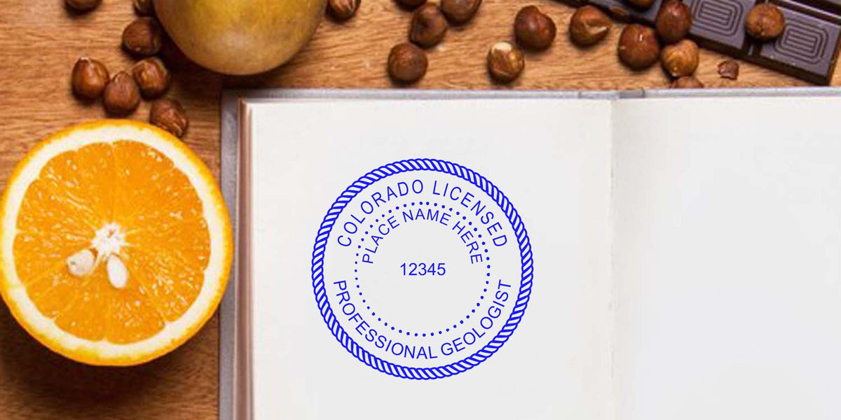 Colorado licensed professional geologist stamp on open notebook with orange, hazelnuts, and chocolate on wooden table, meeting Colorado geologist stamp requirements.