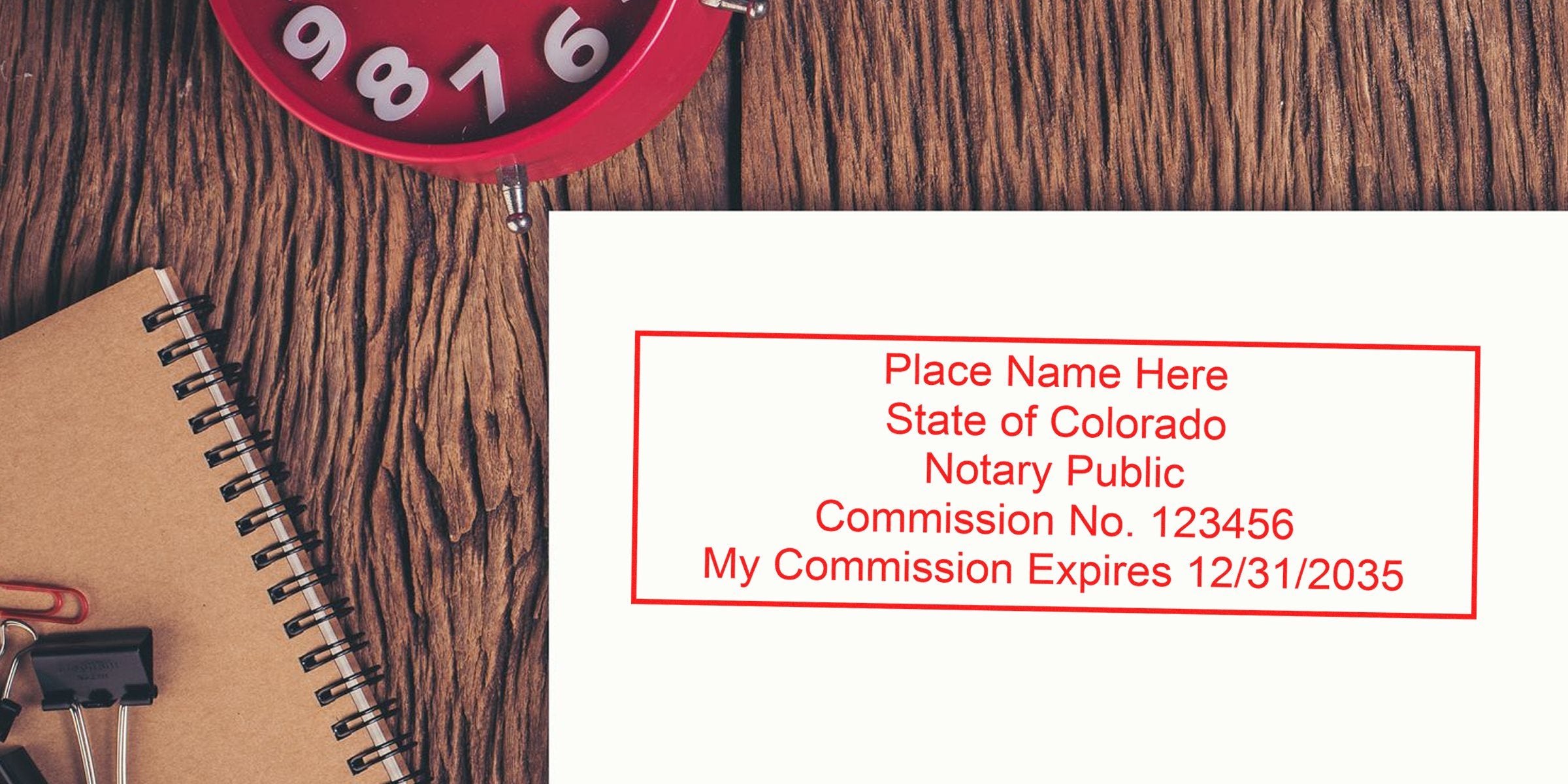 Colorado notary seal with commission number and expiration date on a wooden desk, next to a notebook and red clock, highlighting a top notary seal choice in Colorado.