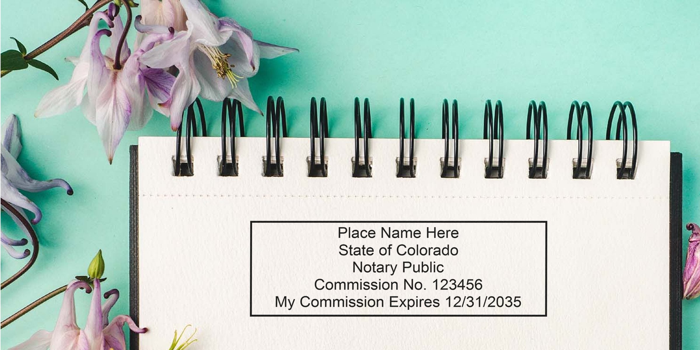 Colorado notary public commission certificate on a spiral notebook with purple flowers on a turquoise background, showing the Colorado notary stamp and key notary stamp requirements.