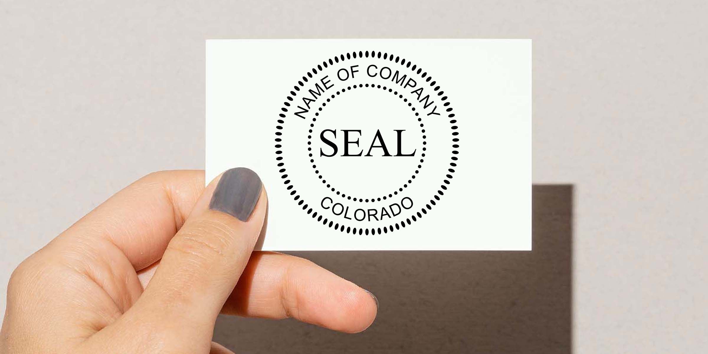 Hand holding a custom company seal stamp card with circular Colorado business logo and “NAME OF COMPANY” text on a clean neutral background
