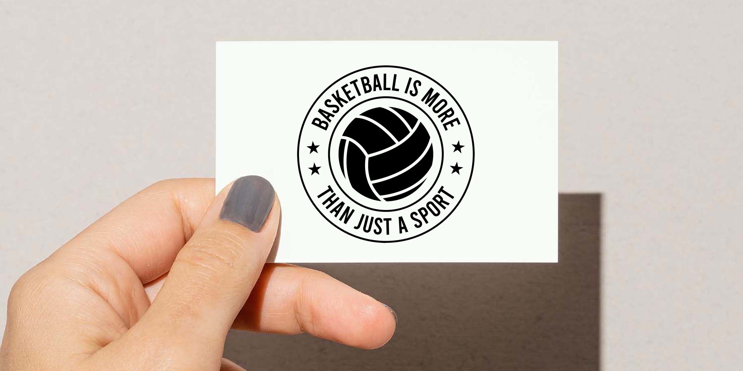 Hand holding a white card with a black basketball emblem and the slogan “Basketball Is More Than Just a Sport” on a clean background