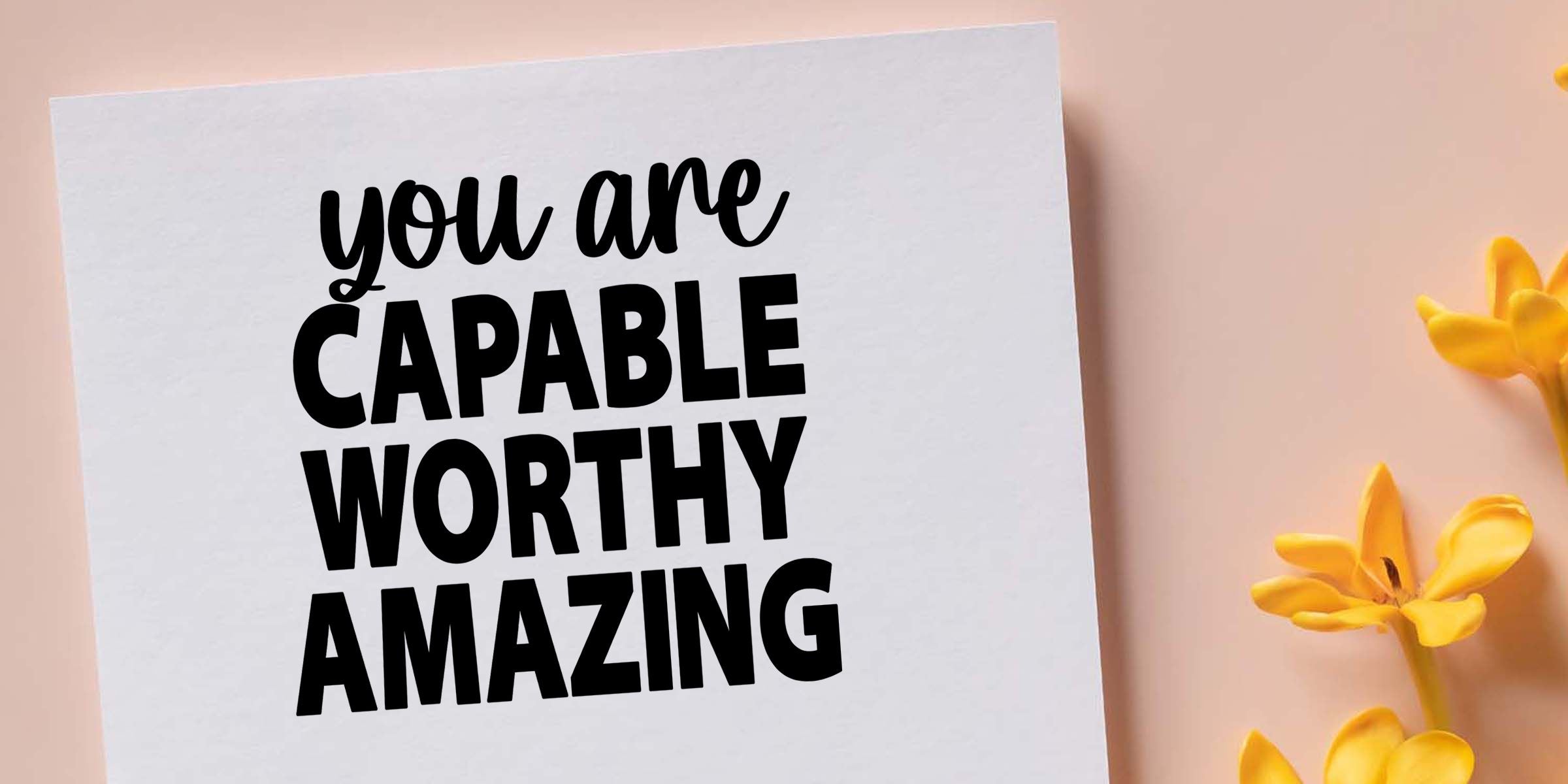 Motivational self-love quote on a white card reading “you are capable worthy amazing” with yellow flowers on a pastel background