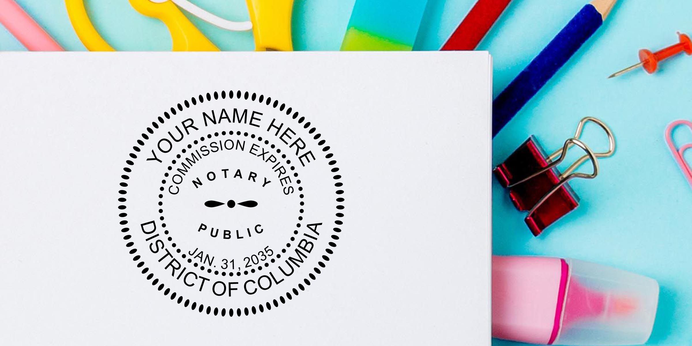 Notary public stamp on white paper with District of Columbia commission seal and colorful office supplies on a blue background, including scissors, binder clip, pushpin, pencil, and sticky notes