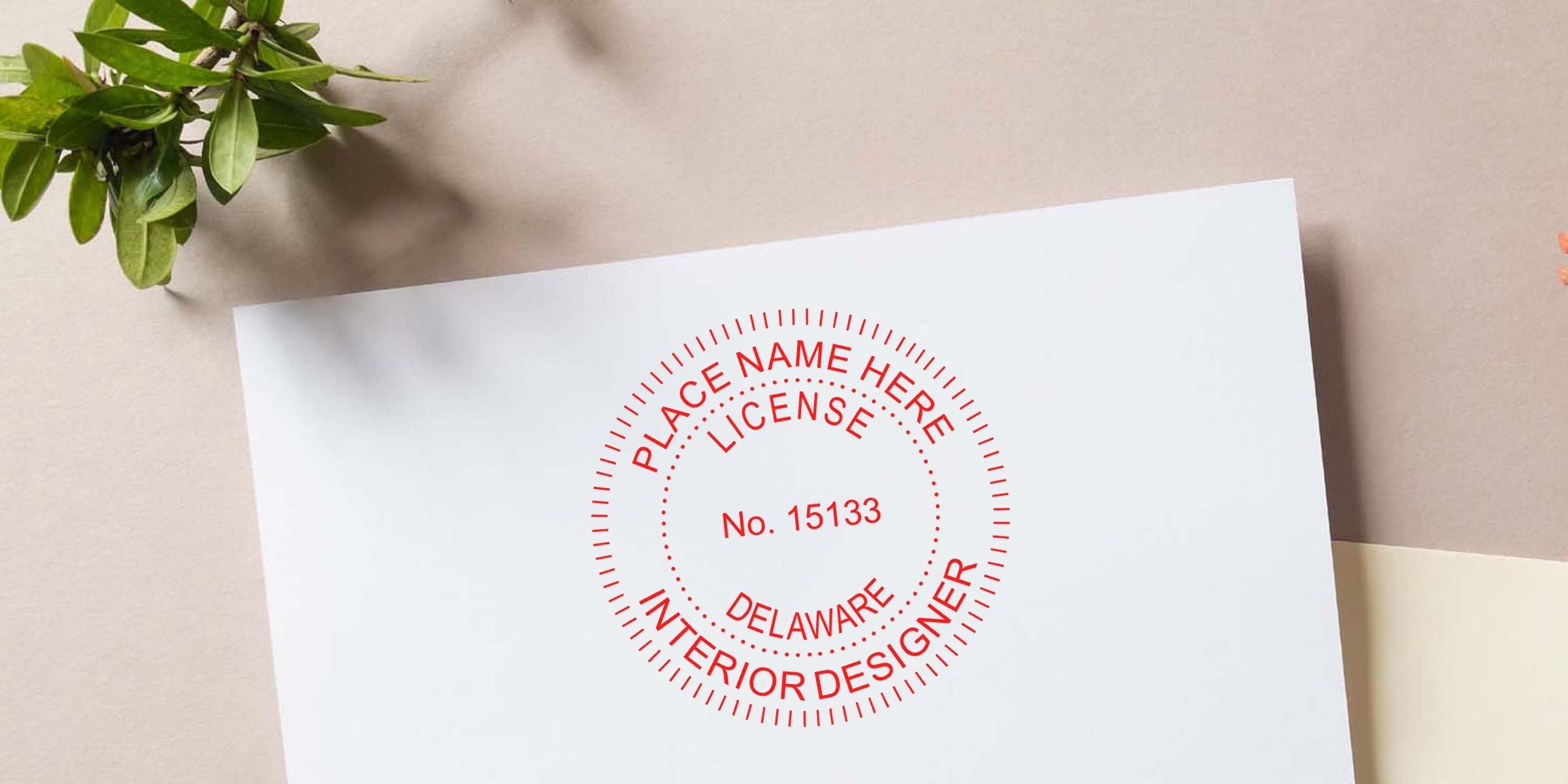 Delaware interior designer license stamp on white paper with green leaves nearby, emphasizing easy Delaware interior designer seal renewal.