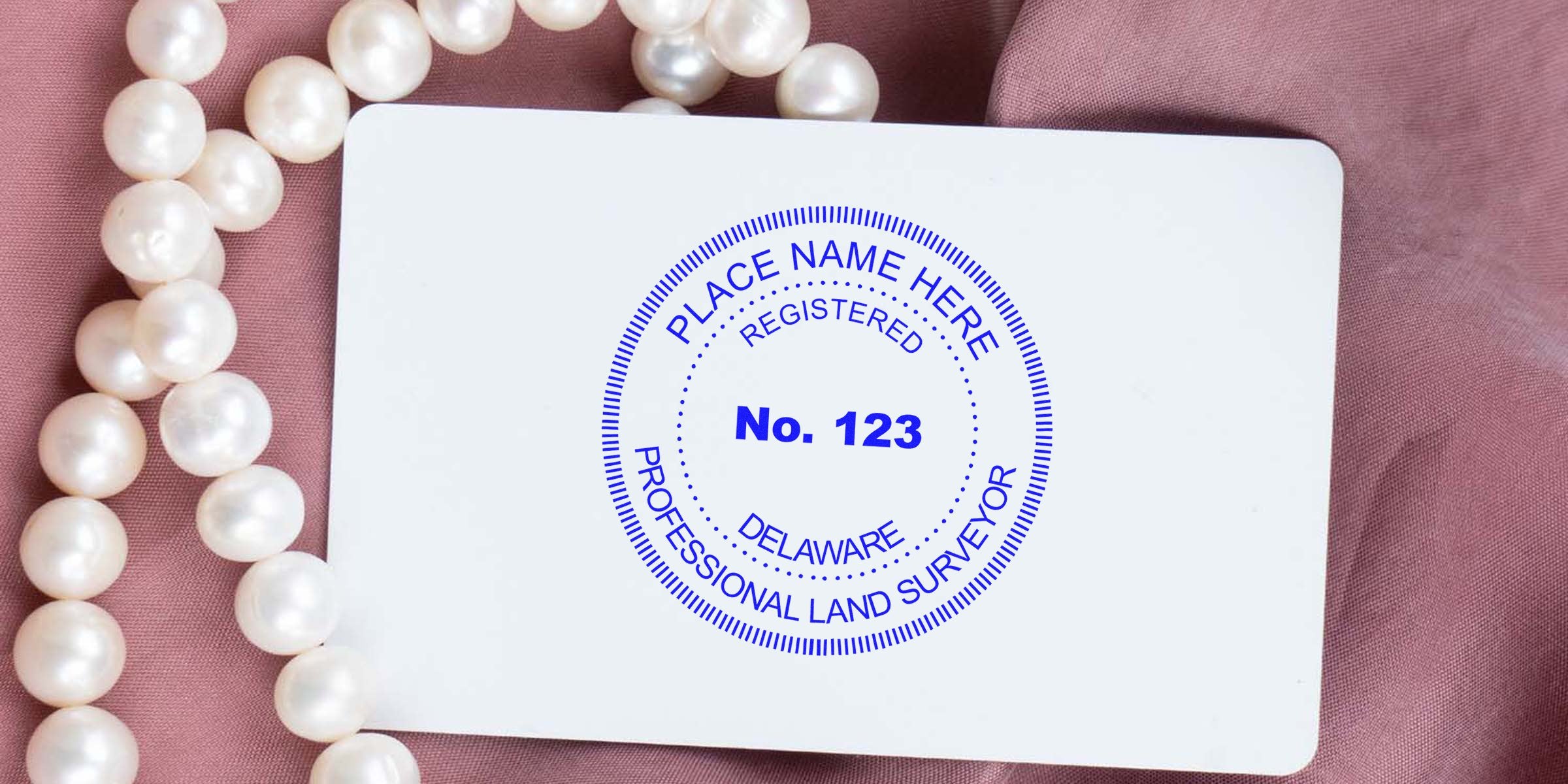 Delaware Surveyor Seal stamp on white card with pearl necklace on pink fabric, highlighting Delaware Surveyor Seal requirements.