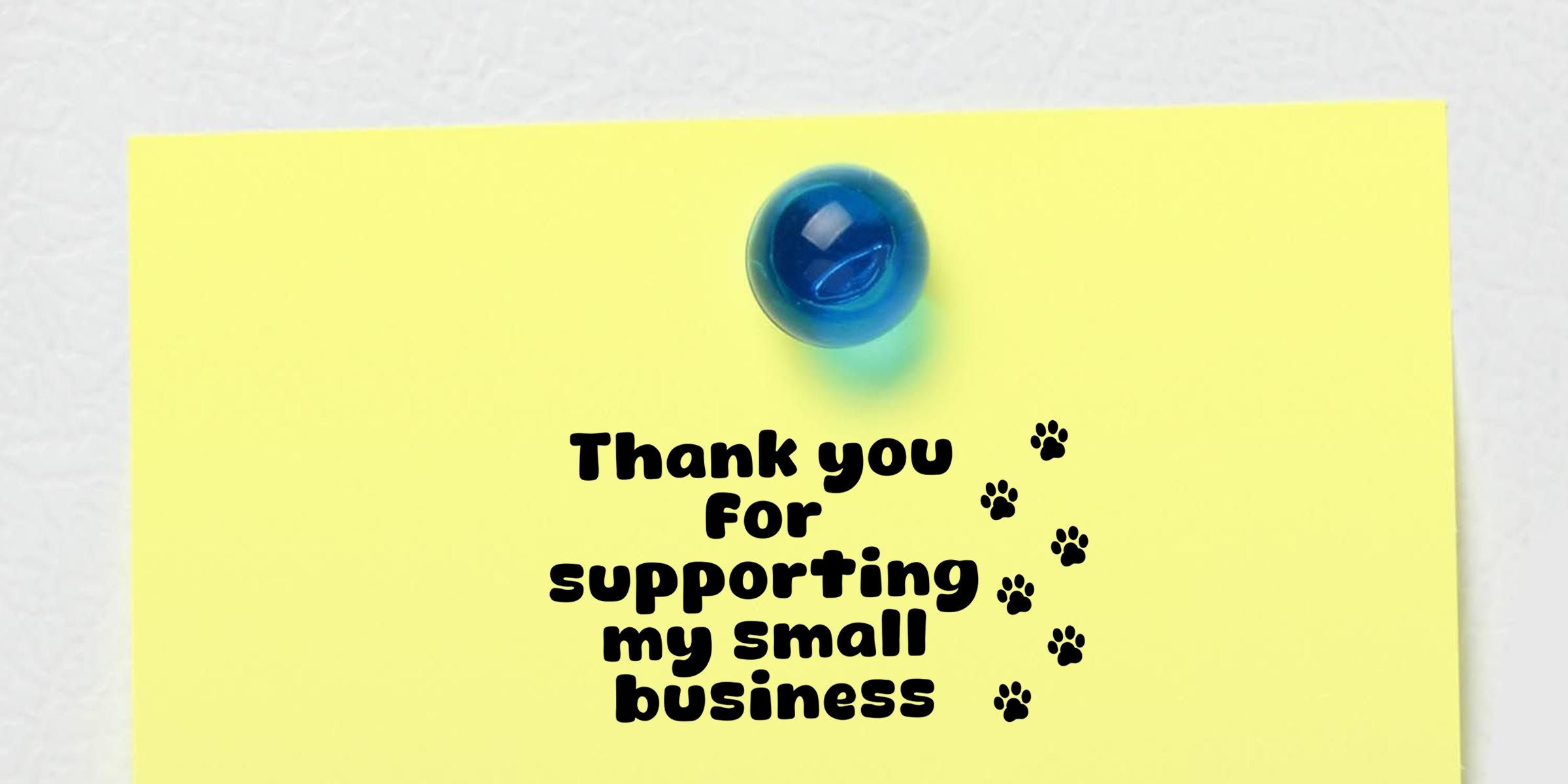 Yellow thank you note with paw prints reading “Thank you for supporting my small business,” pinned with a blue pushpin on a white background