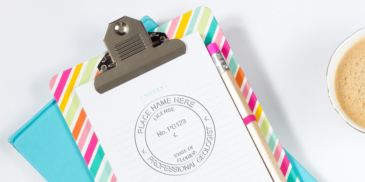 Clipboard with professional geologist license template, pencil, notebook, and coffee cup on white desk for Florida Geologist Stamp exam prep and requirements.