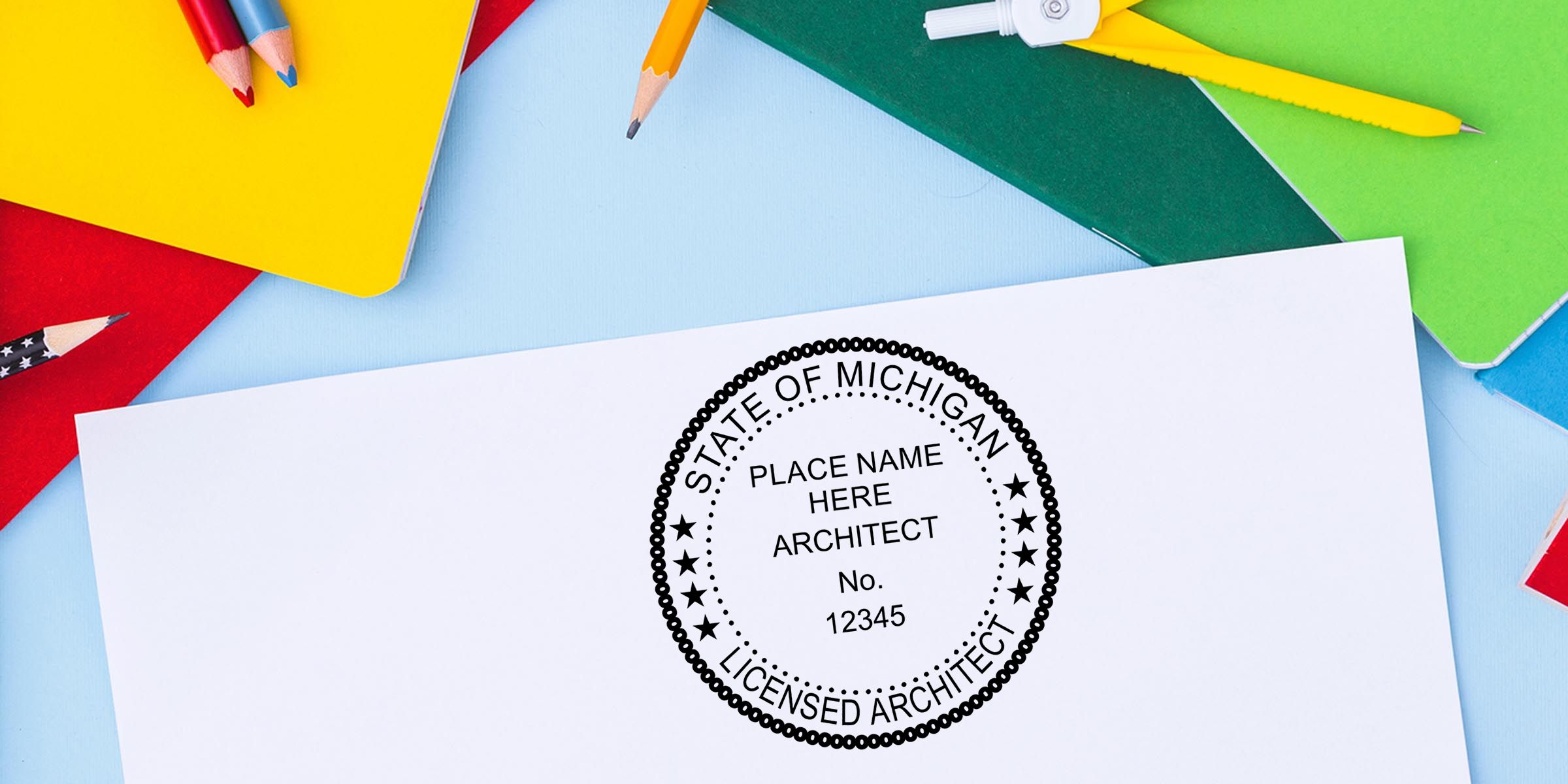 Licensed architect stamp for State of Michigan on white paper surrounded by colorful pencils and notebooks on a blue background