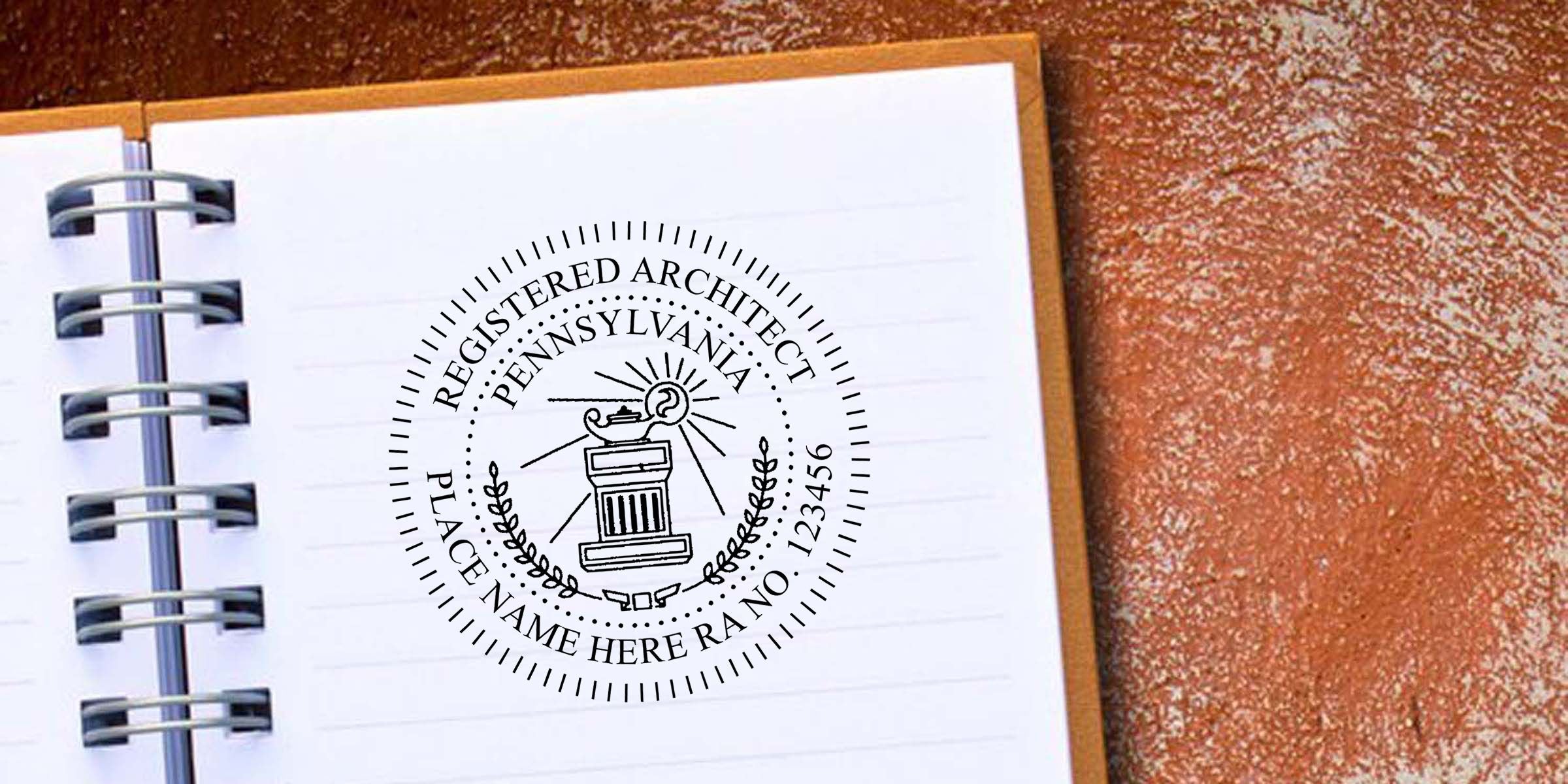 Pennsylvania Registered Architect seal on a spiral-bound notebook page with a blank logo space and metal binder rings on a textured brown background