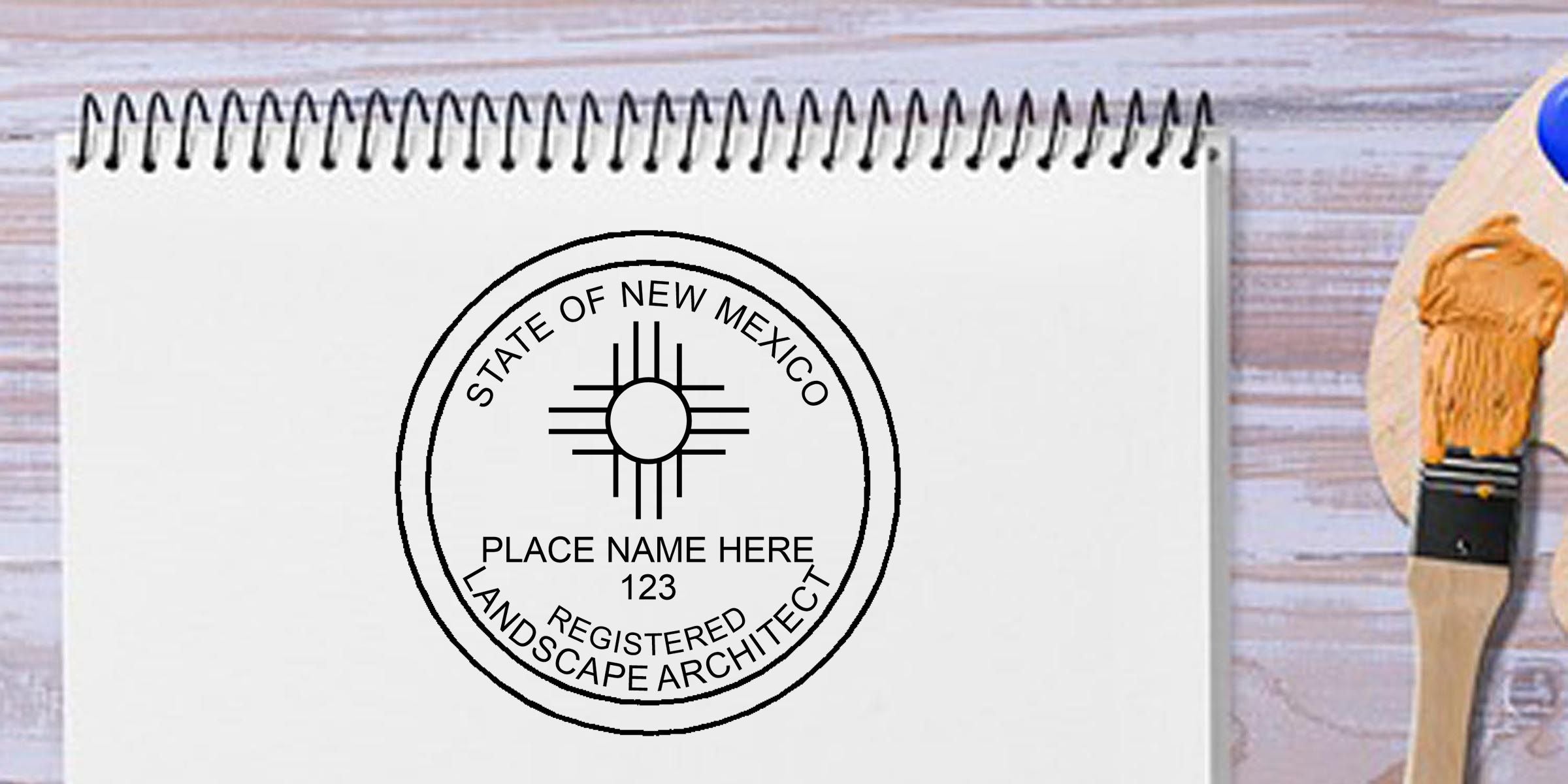 Custom New Mexico registered landscape architect seal on a spiral notebook with “Place Name Here” text and a paintbrush on a wooden background