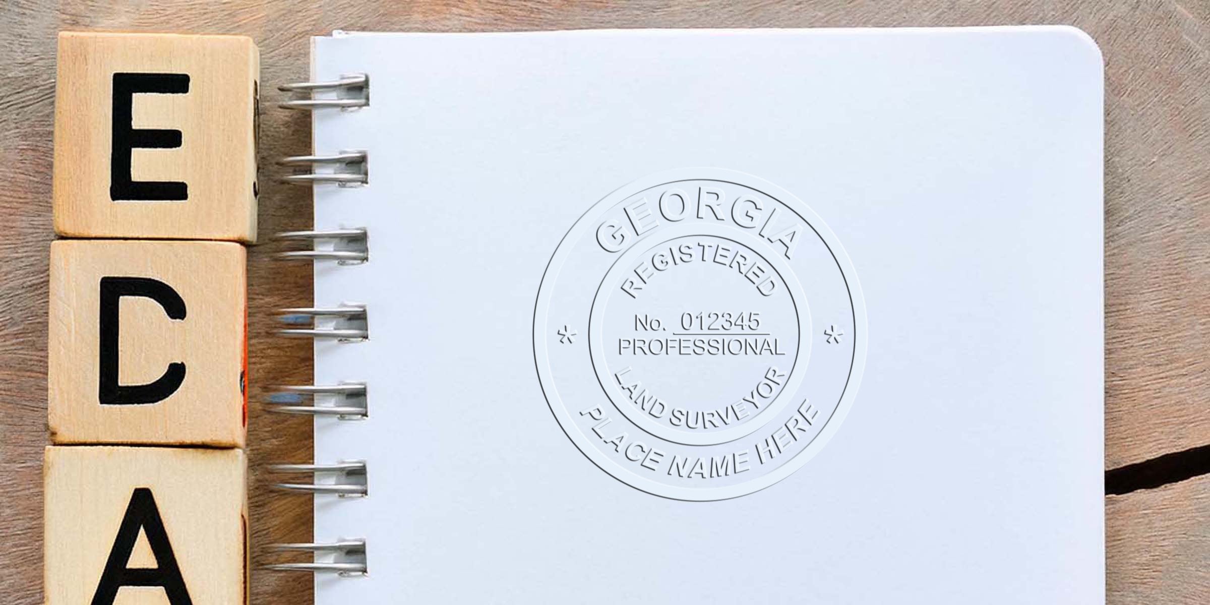 Wooden blocks spelling ECPA sit beside a spiral notebook embossed with a Georgia land surveyor seal, highlighting the seal's specifications.