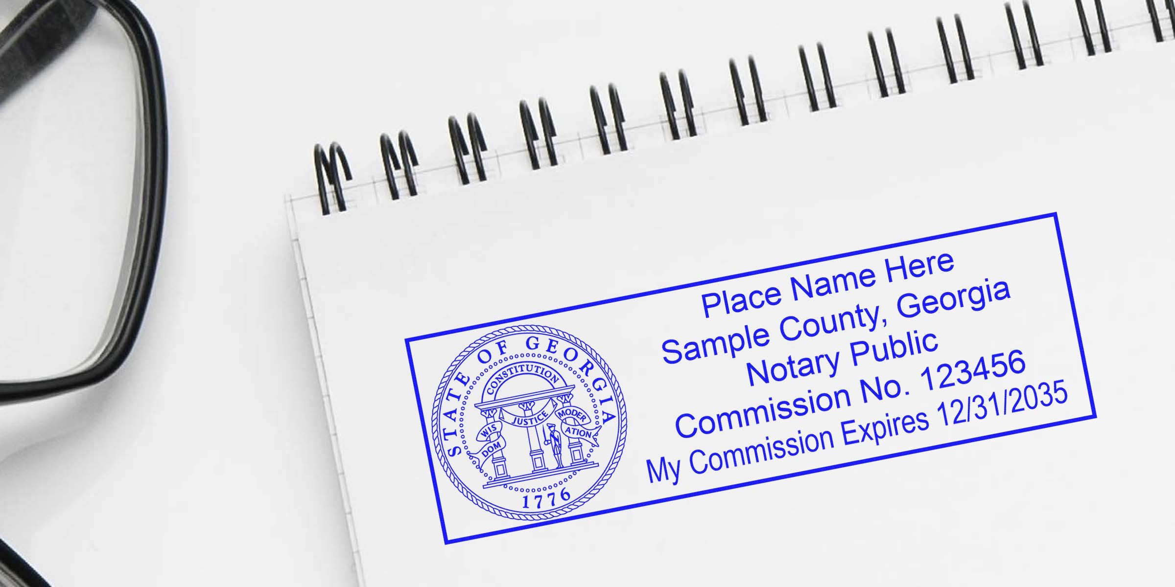 Georgia notary stamps on a spiral notebook with eyeglasses nearby, highlighting budget-friendly notary supplies.
