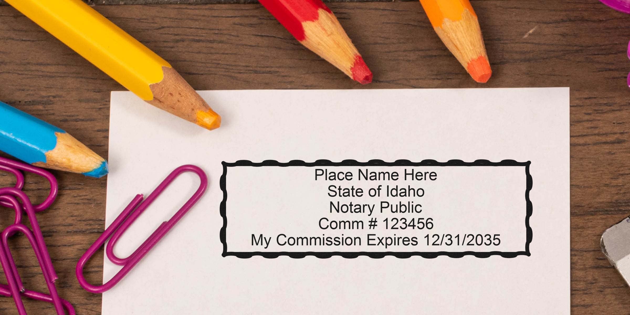 Idaho notary public stamp on paper with commission number and expiration date, surrounded by colored pencils and pink paper clips, highlighting Idaho notary seal size and dimensions.