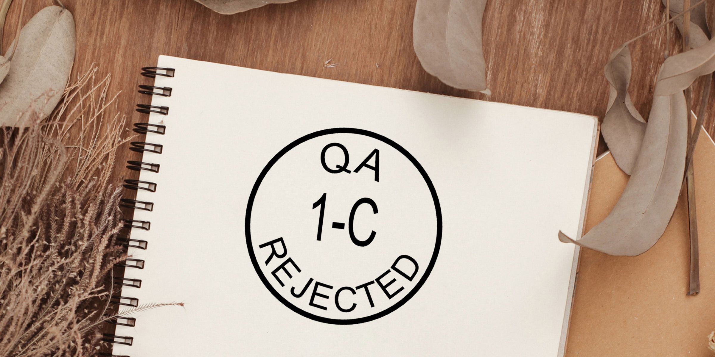 QA rejected stamp on a spiral notebook with a wooden background and dried leaves, showing quality assurance inspection failure notice