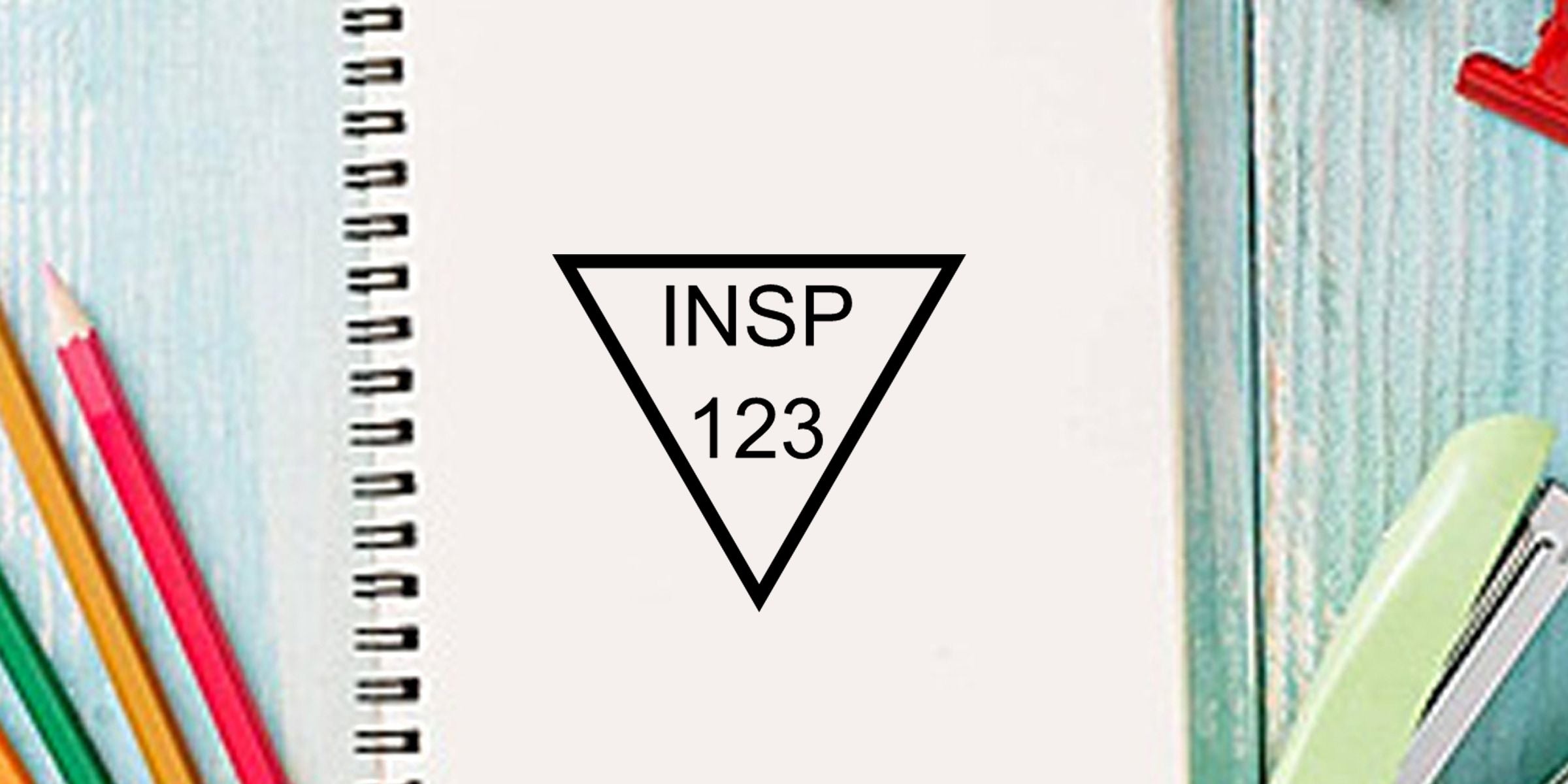 Spiral notebook with colorful pencils and stationery surrounding a blank page featuring an INSP 123 triangle logo, creative school supplies background