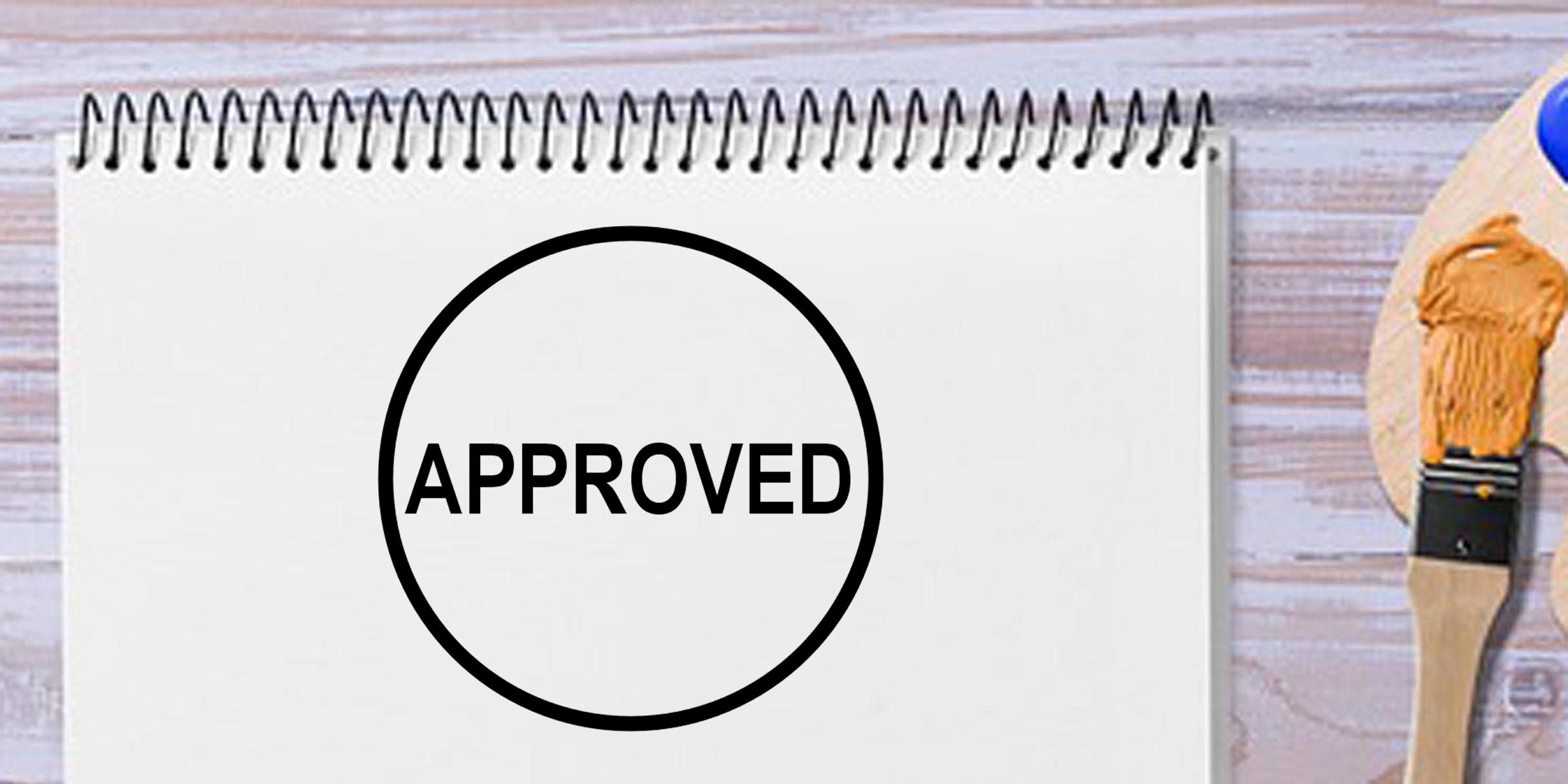 Approved stamp on a blank spiral notebook with a paintbrush on a wooden desk