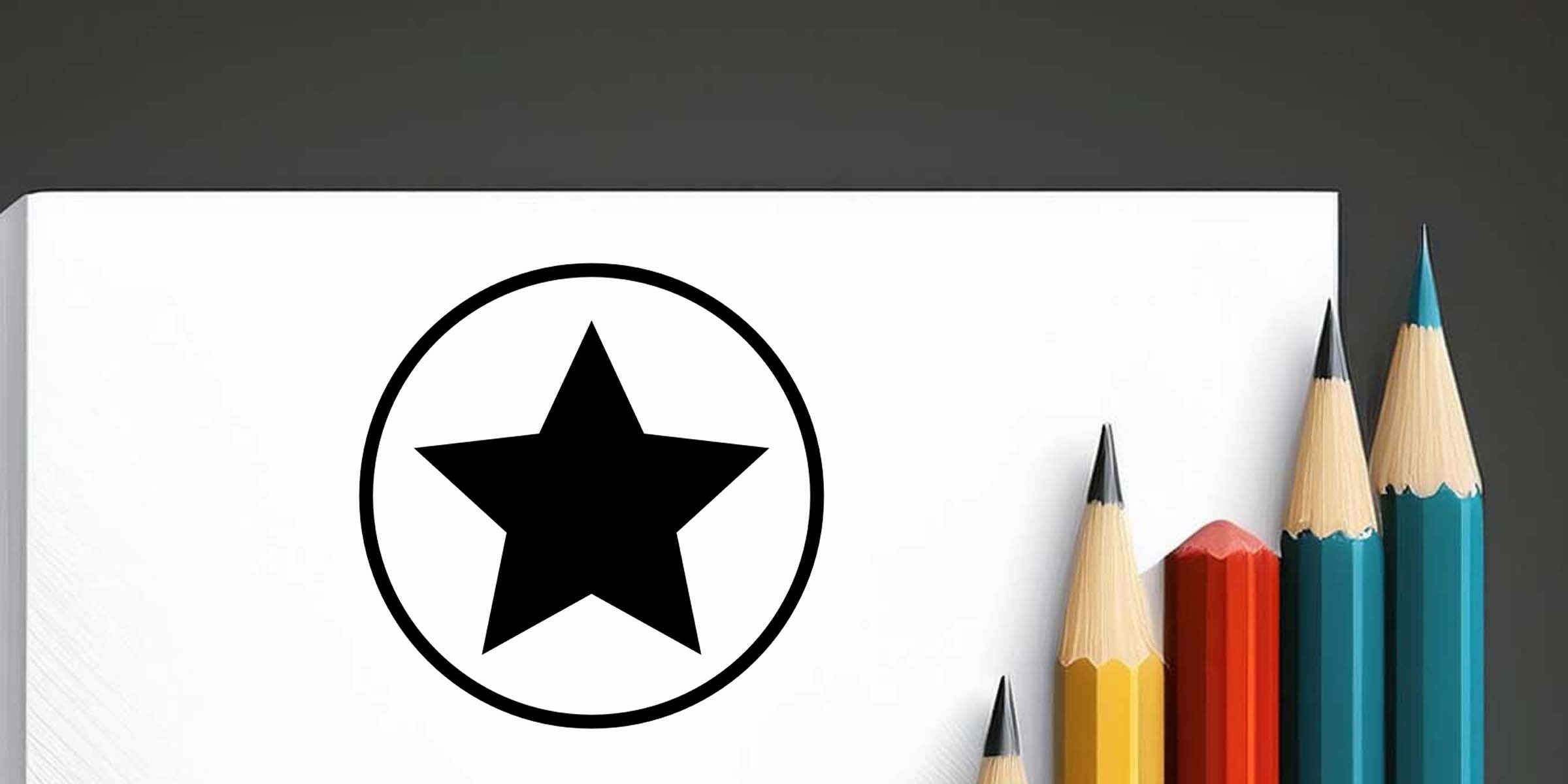 Black star icon inside a circle on a white notebook cover with colorful sharpened pencils arranged beside it on a dark background