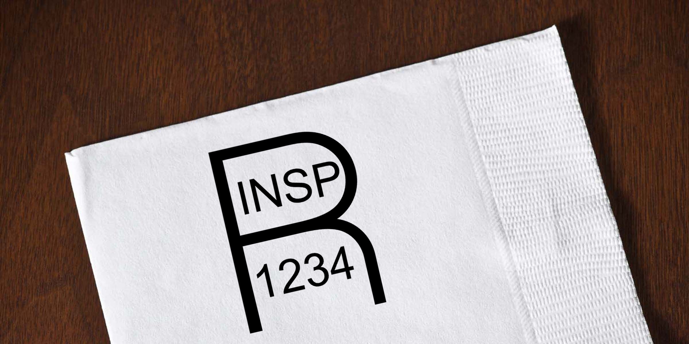 White cocktail napkin on a wooden table featuring the black INSP 1234 logo design