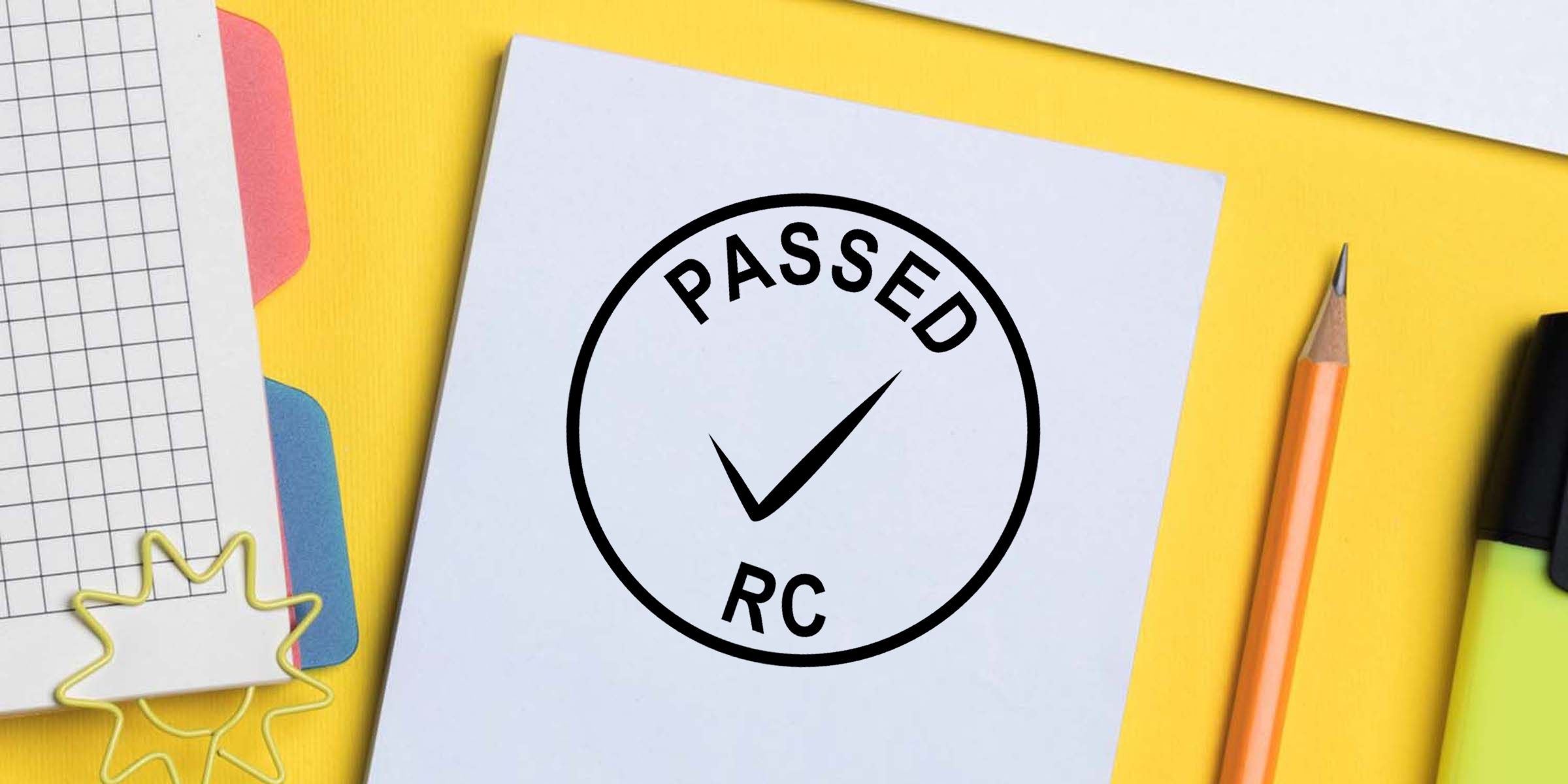Passed stamp with checkmark on white paper surrounded by colorful office stationery on a yellow desk