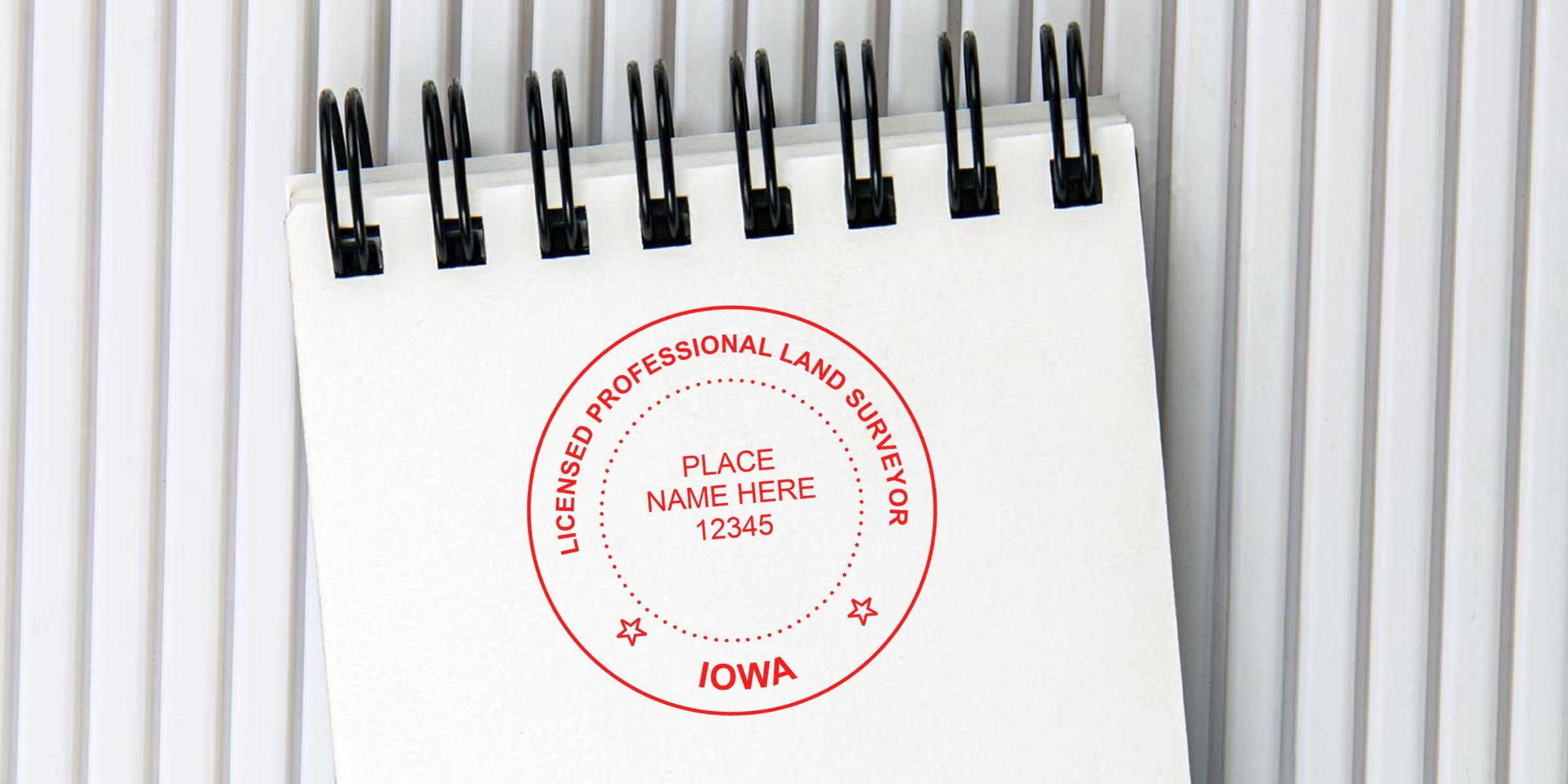 Licensed professional land surveyor stamp on white spiral notebook in Iowa, displaying stamp size and dimensions.