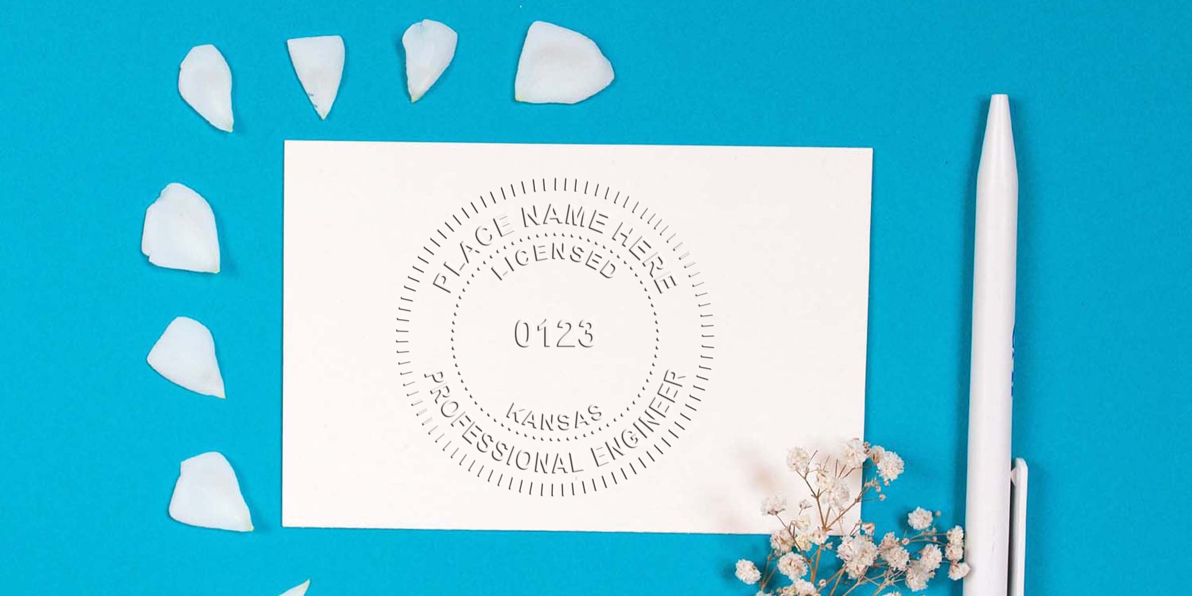 Kansas engineer stamp and licensed professional engineer seal on white card with pen and flower petals on blue background, made by a professional stamp maker.