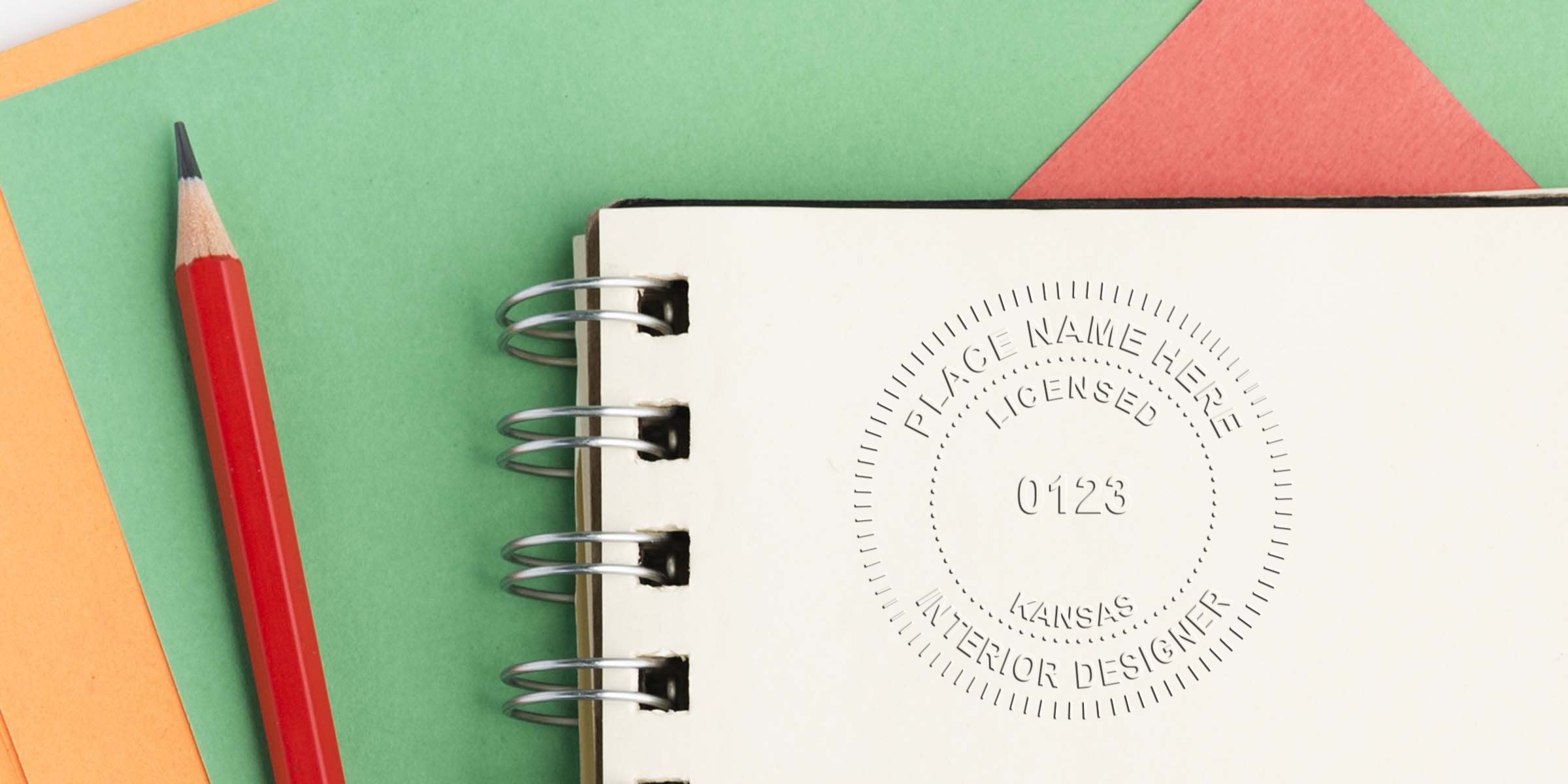 Red pencil on colorful paper with spiral notebook showing embossed Kansas interior designer license and licensing stamp.