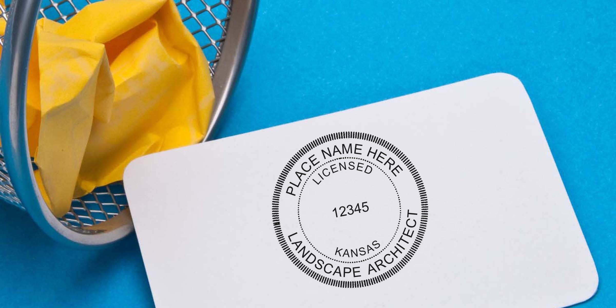 Custom Kansas landscape architect stamp on white card with yellow paper in metal trash bin against blue background.