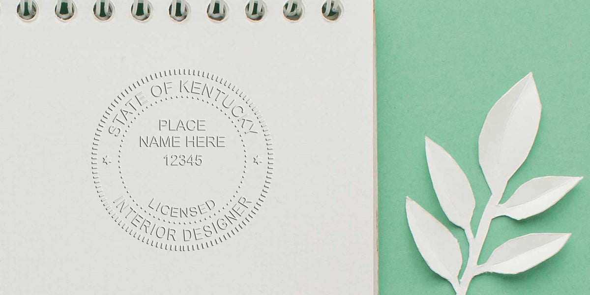 Licensed interior designer seal on notebook with paper leaves on green background, emphasizing Kentucky interior design standards and stamp requirements.