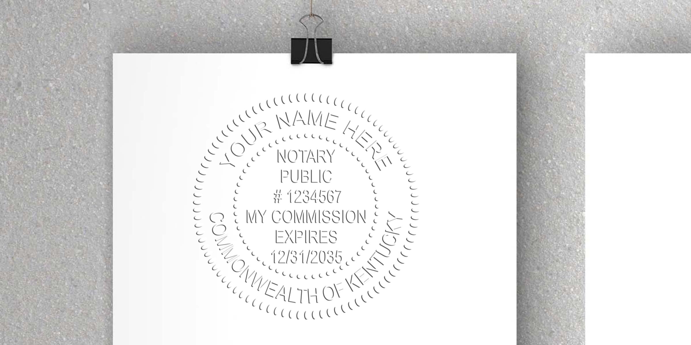 Kentucky notary public stamp with commission expiration date on white paper clipped to gray wall, symbolizing Kentucky notary supplies and the steps to become a notary in Kentucky.