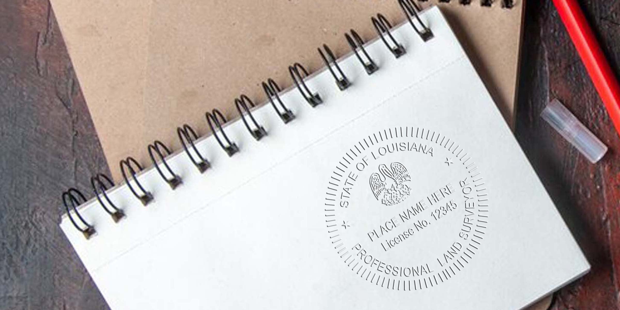 Spiral notebook with Louisiana land surveyor seal and specifications, accompanied by a red pen on a wooden desk.
