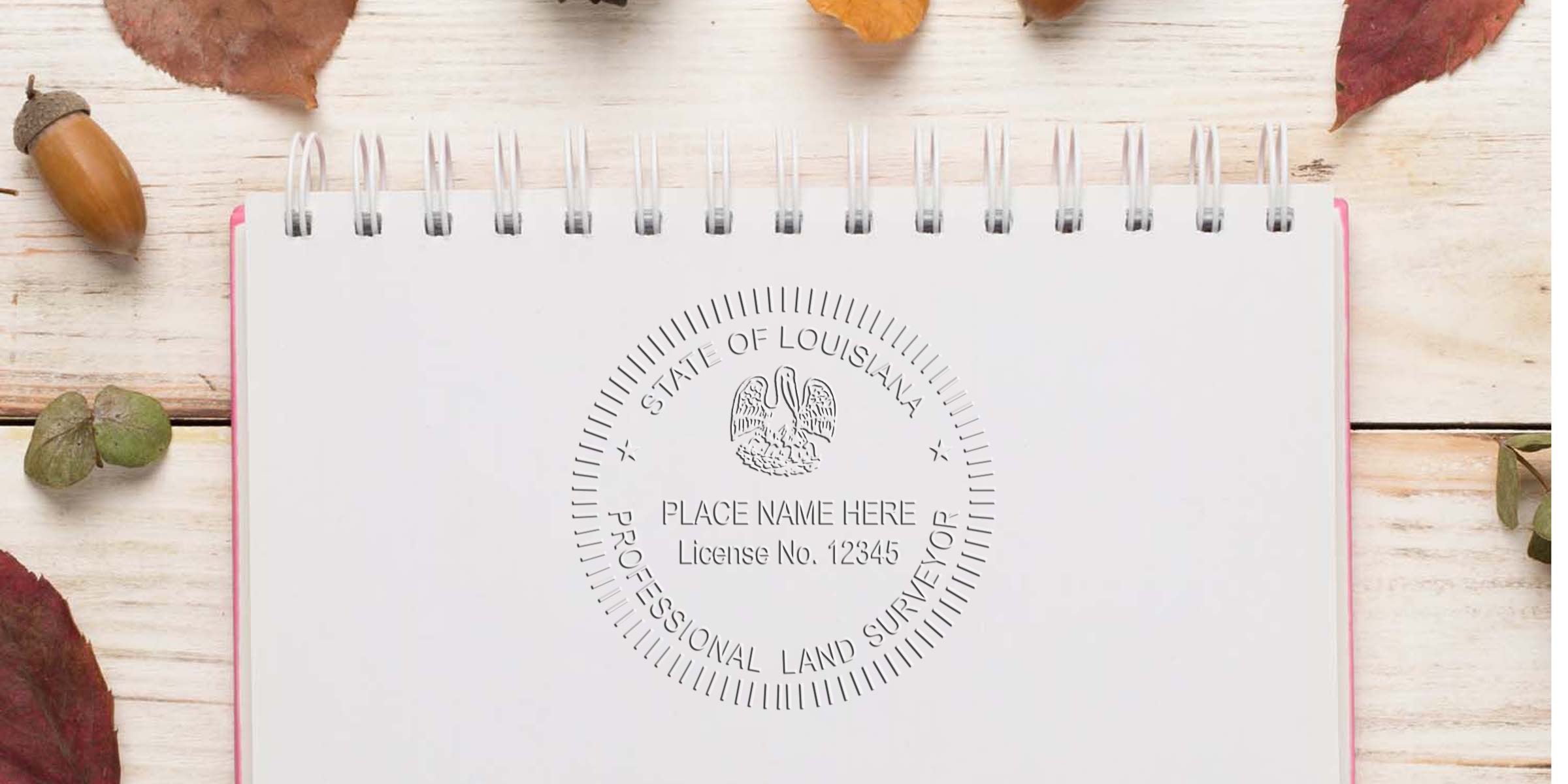 Louisiana land surveyor seal embossed on white notebook with autumn leaves and acorn on wooden table, showing land surveyor embosser.