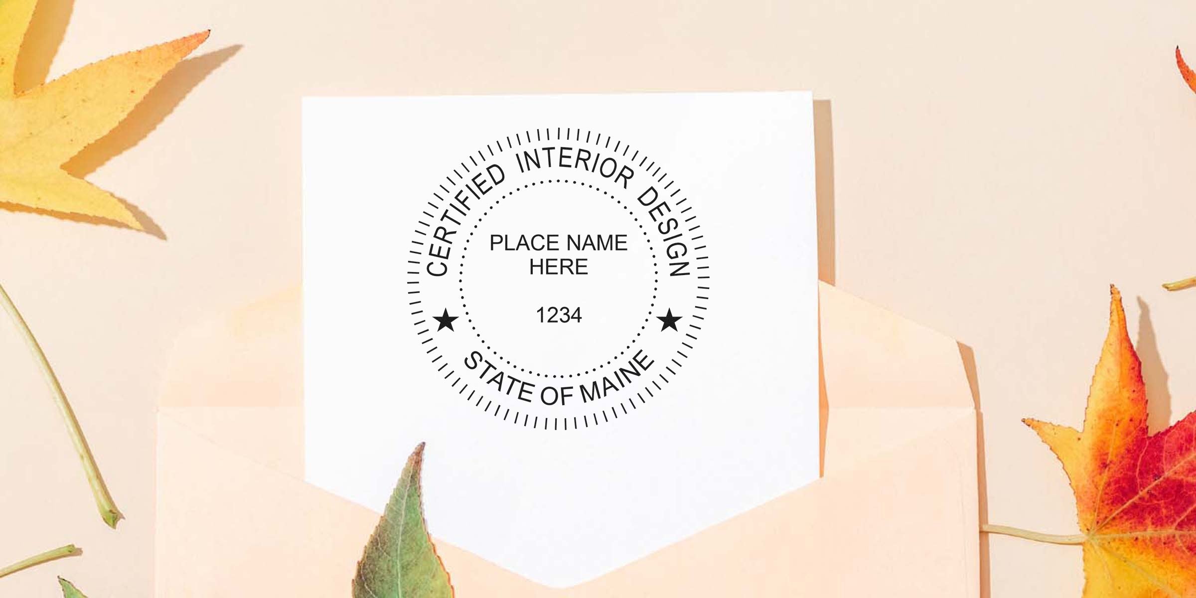Seal embosser imprint of certified Maine interior designer on white paper with autumn leaves and an envelope in the background.