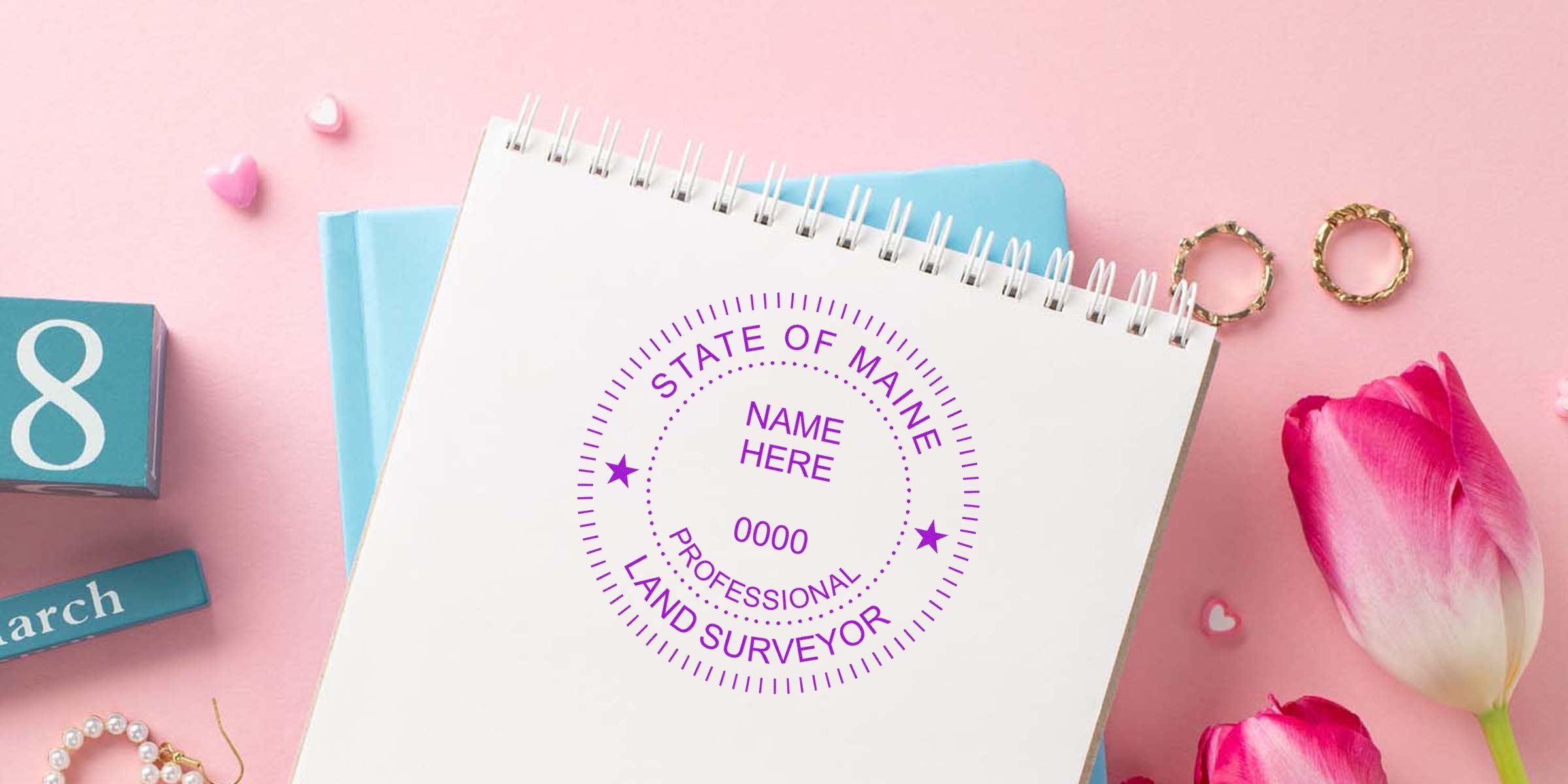 Maine land surveyor stamp on notebook with pink tulips and gold rings on pastel background, showing surveyor stamp design checklist.