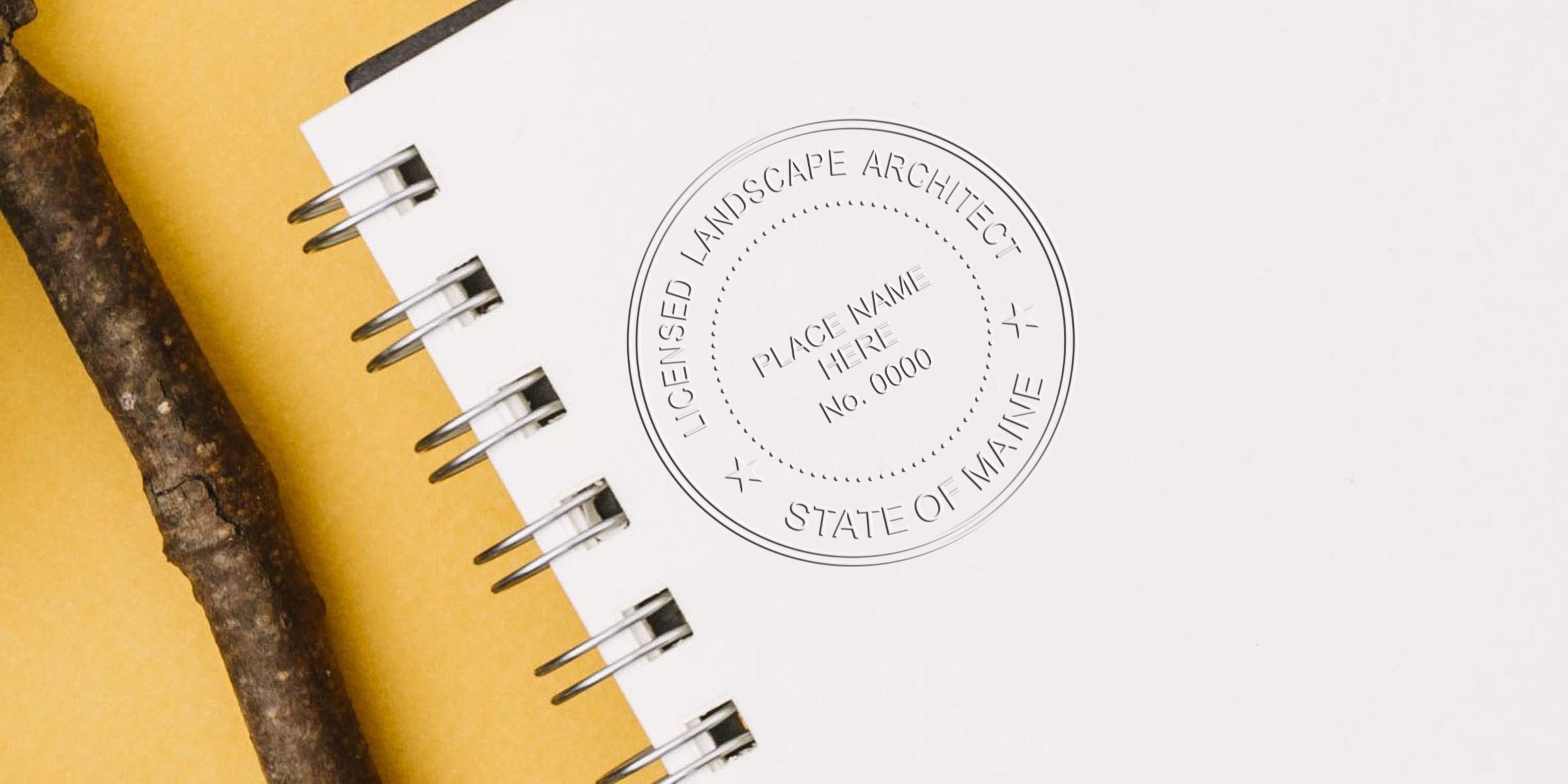 Spiral notebook with Maine landscape architect stamp and natural wooden stick on yellow background, emphasizing Maine landscape architect licensing requirements.