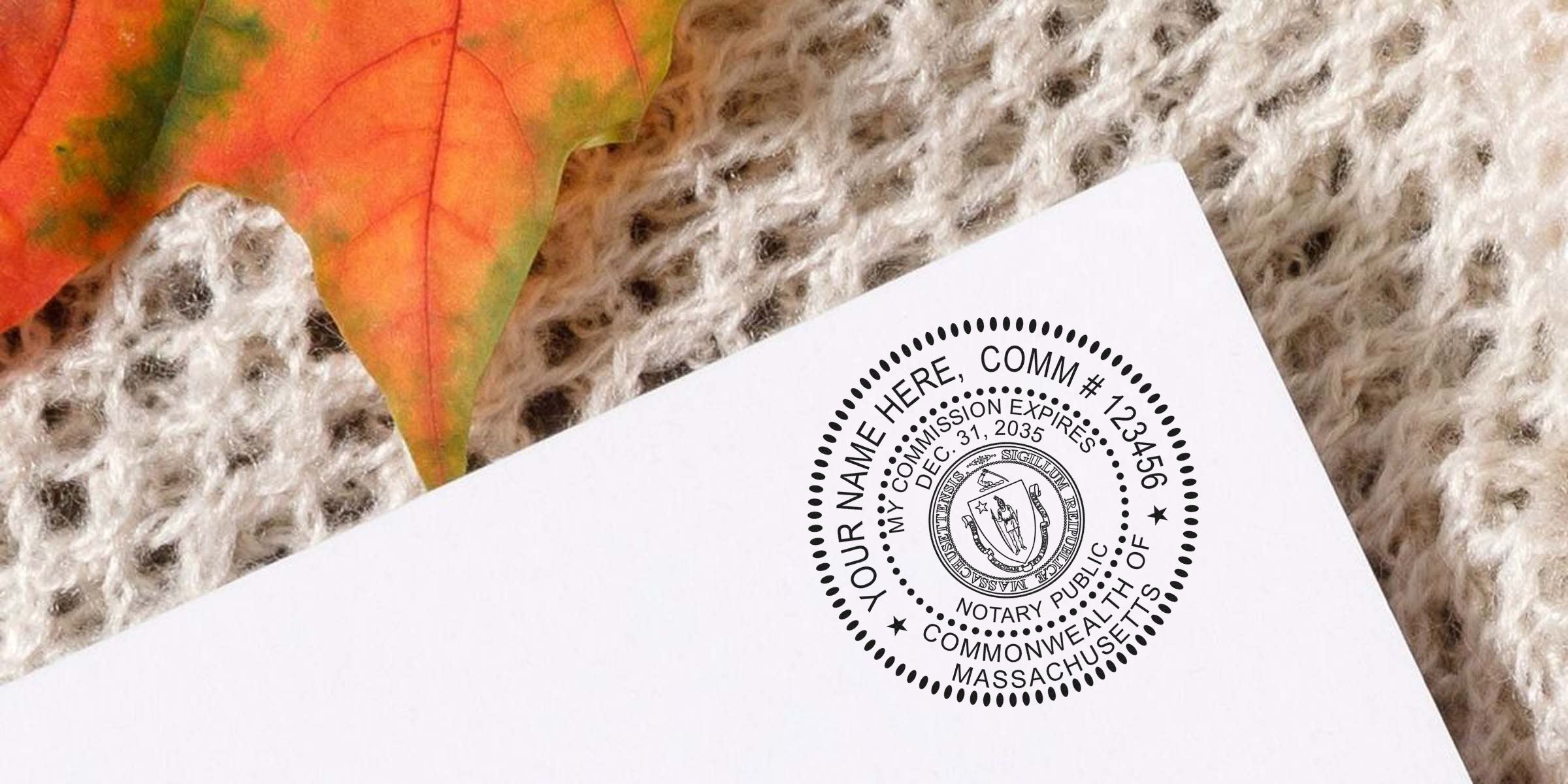 Massachusetts Notary Stamp MA on white paper with autumn leaf and knitted fabric background, showcasing a Perfect Notary Stamp Massachusetts design.