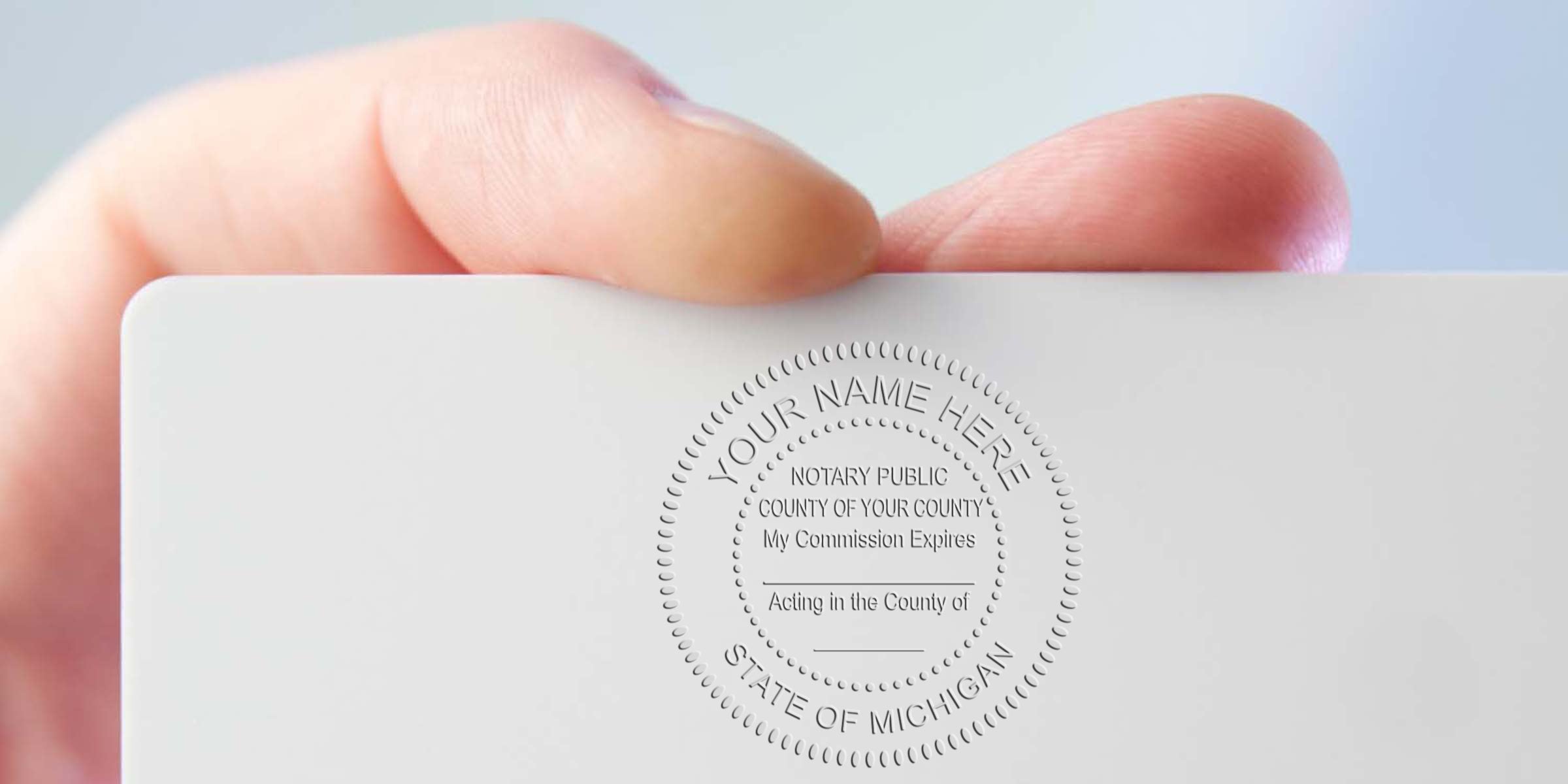 Hand holding a white card with a Michigan Notary Stamp showing the Official Notary Seal embossed.