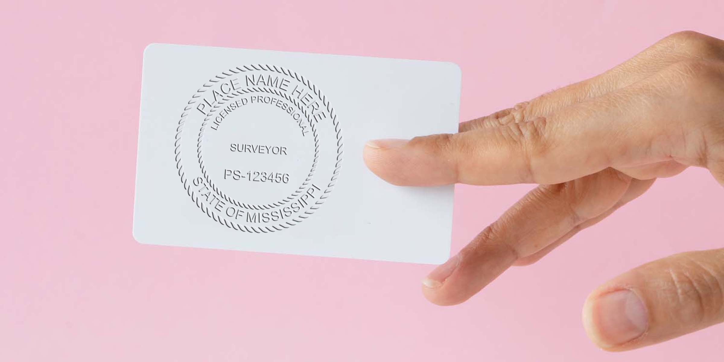 Hand holding Mississippi-licensed surveyor card showing license number on pink background, with Mississippi land surveyor stamp and custom surveyor seal.