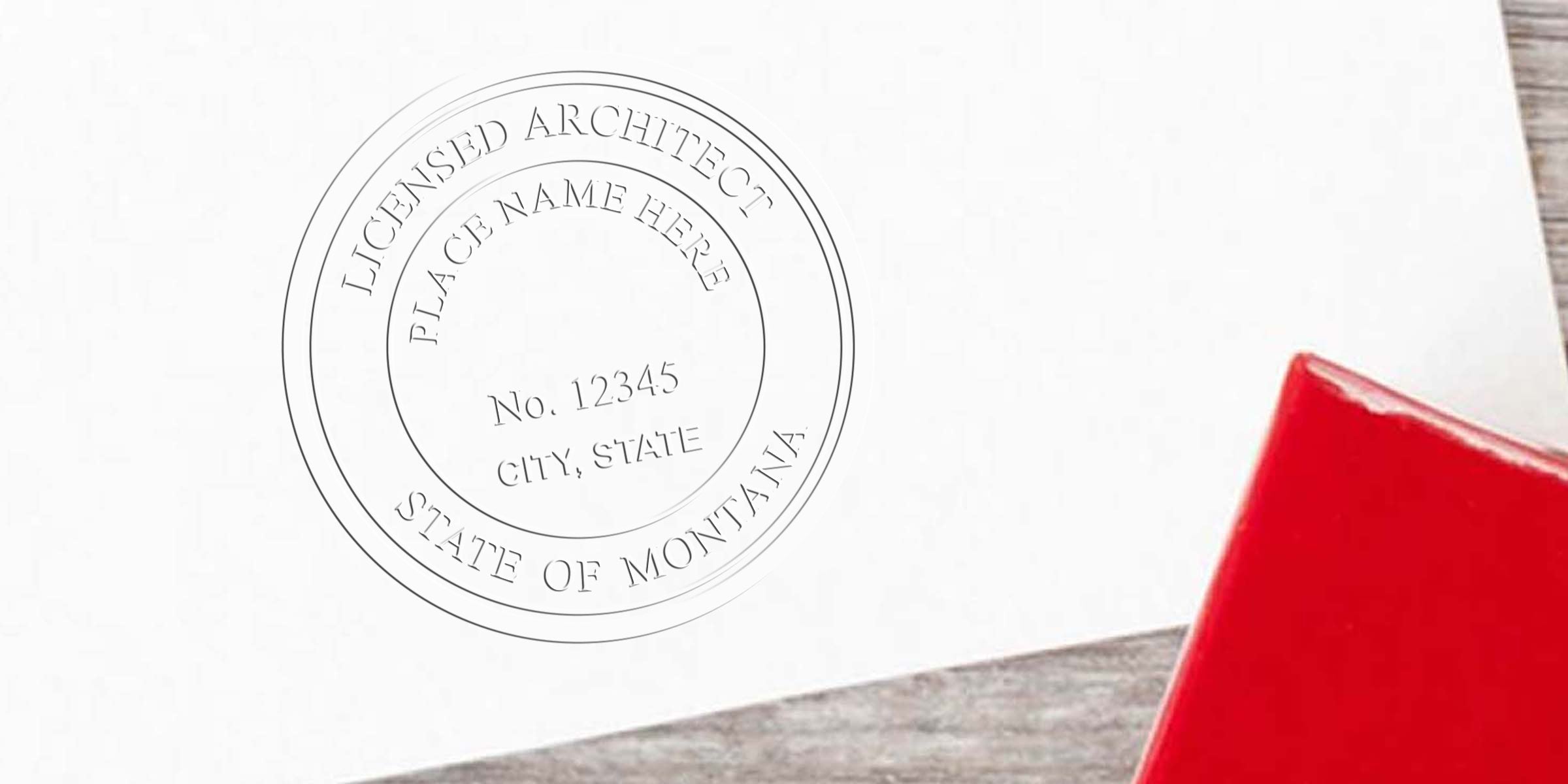 Montana architect stamp on white paper with licensed architect stamp and red folder on wooden table, meeting Montana architect stamp requirements.